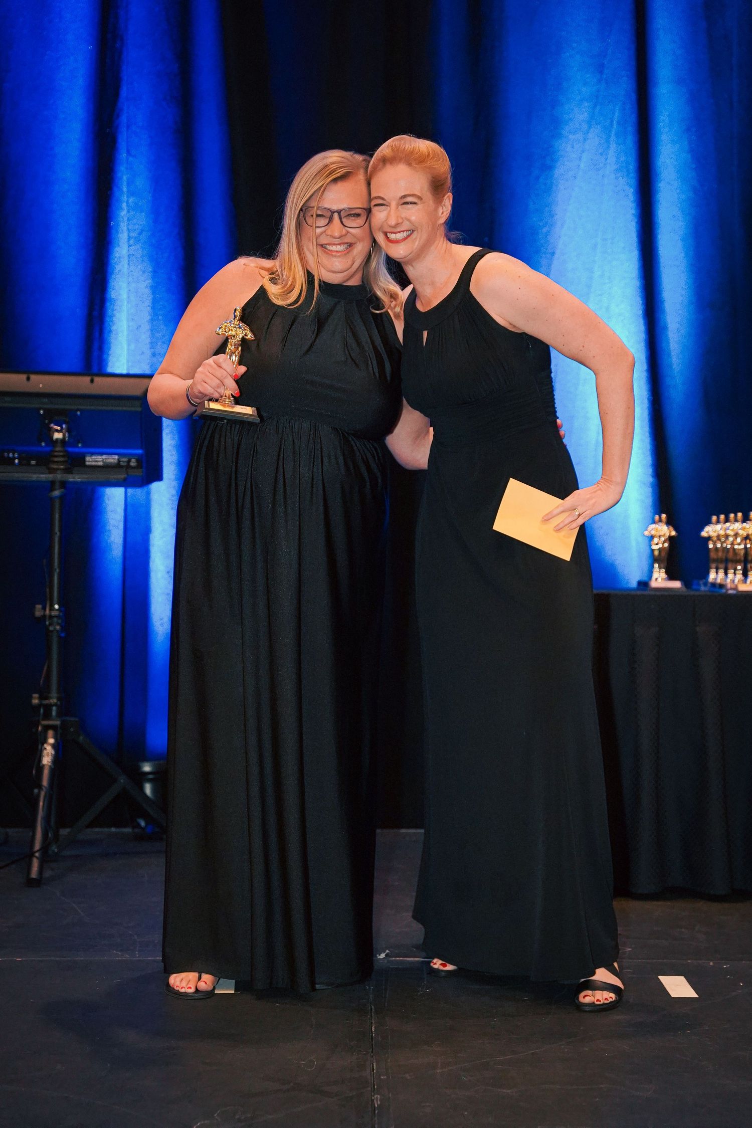 Colleagues pose together on stage during an evening awards ceremony with blue lighting.