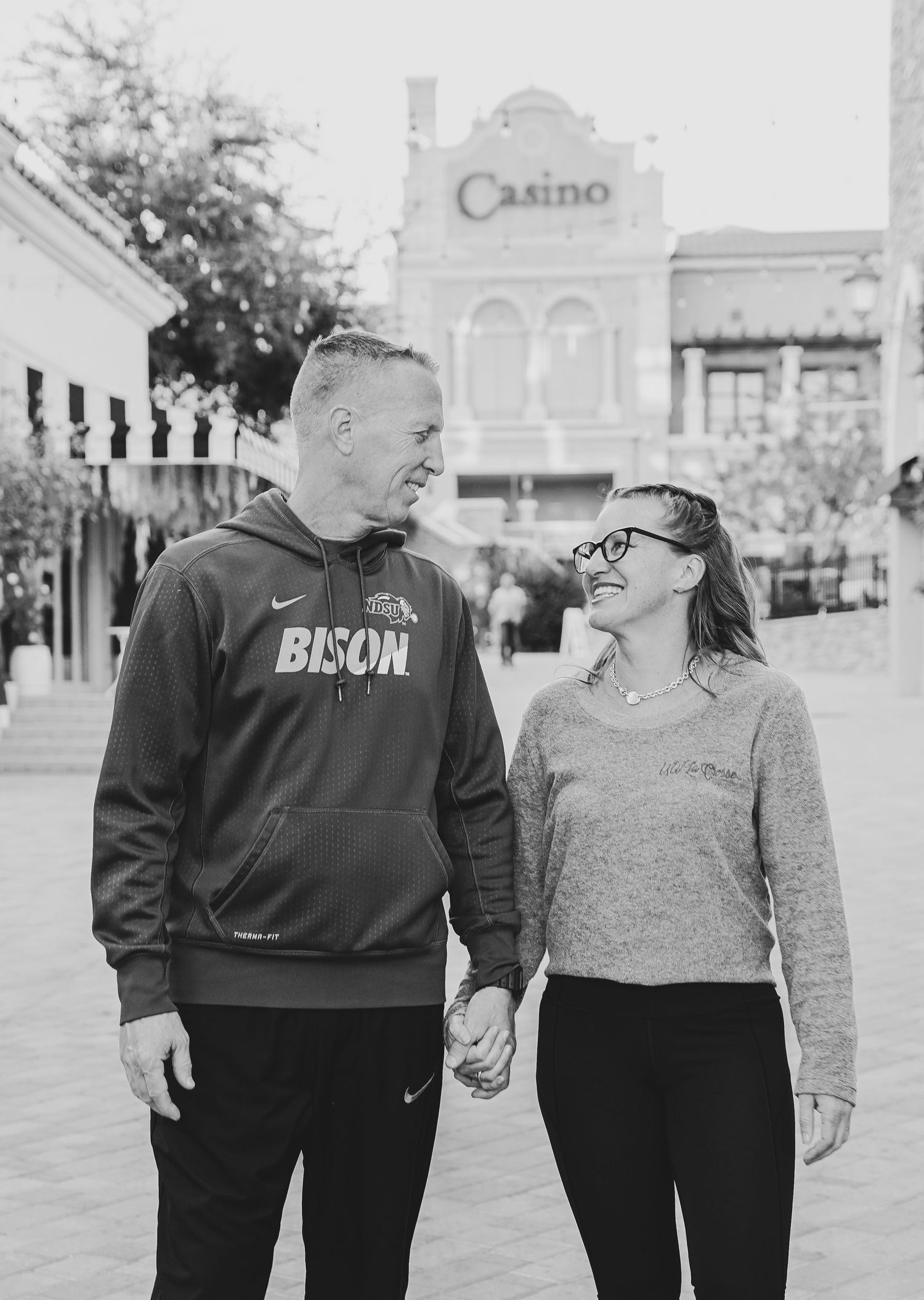 Black and white photo showing a couple in casual wear smiling at each other in front of a casino building.