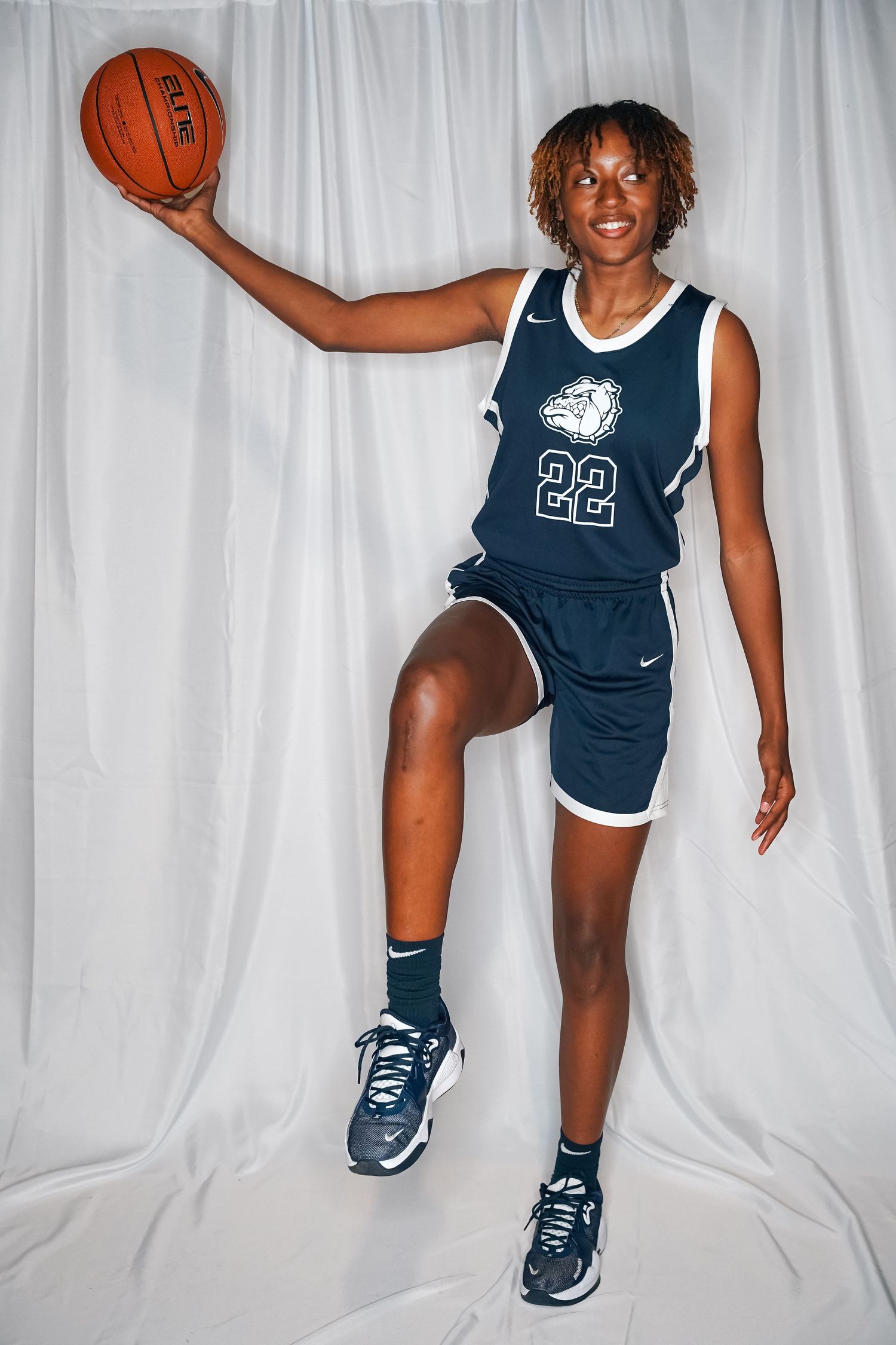 Basketball player wearing navy jersey number 22 poses with ball against white backdrop.