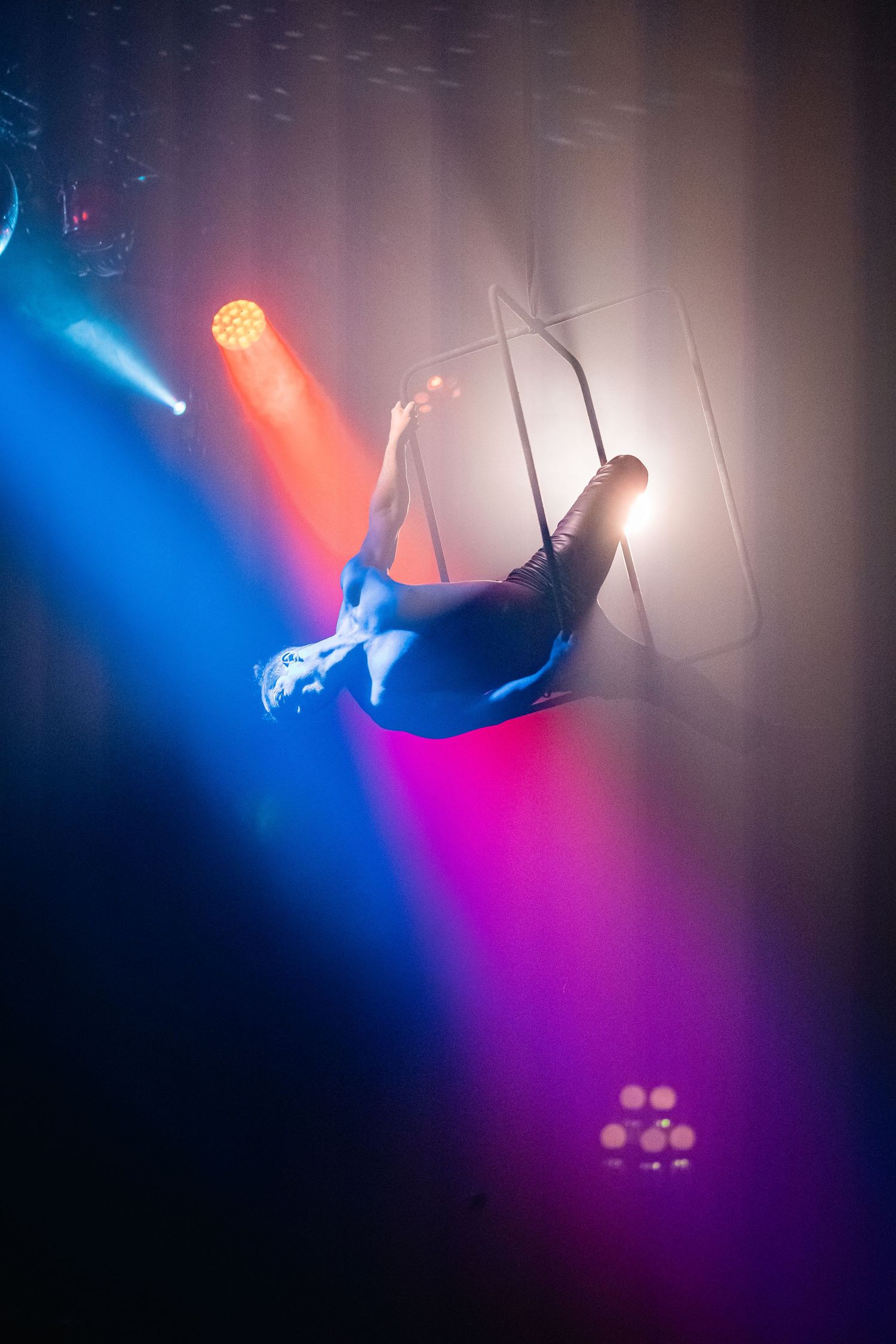 Aerial acrobat performing in dramatic blue and red spotlights on stage.