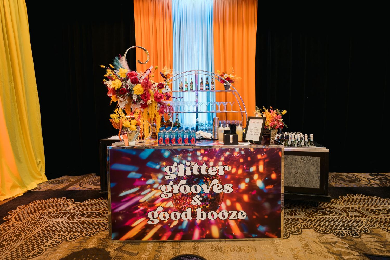 Illuminated bar setup with colorful drapes and floral arrangements for an elegant casino event.