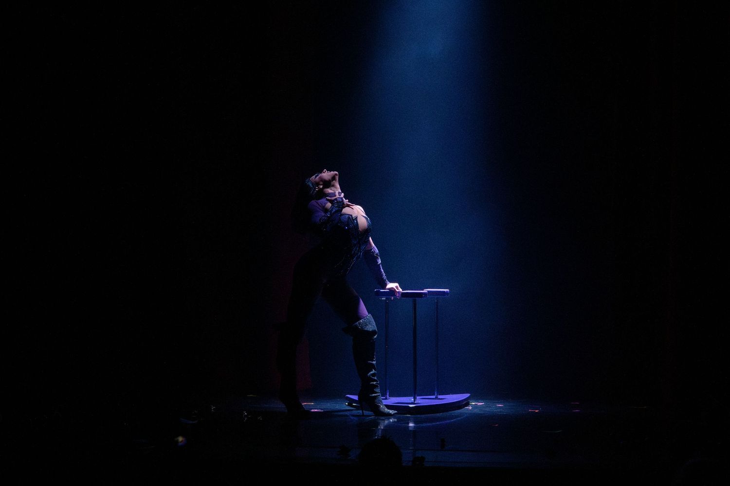Solo performer stands in dramatic blue spotlight on dark stage.