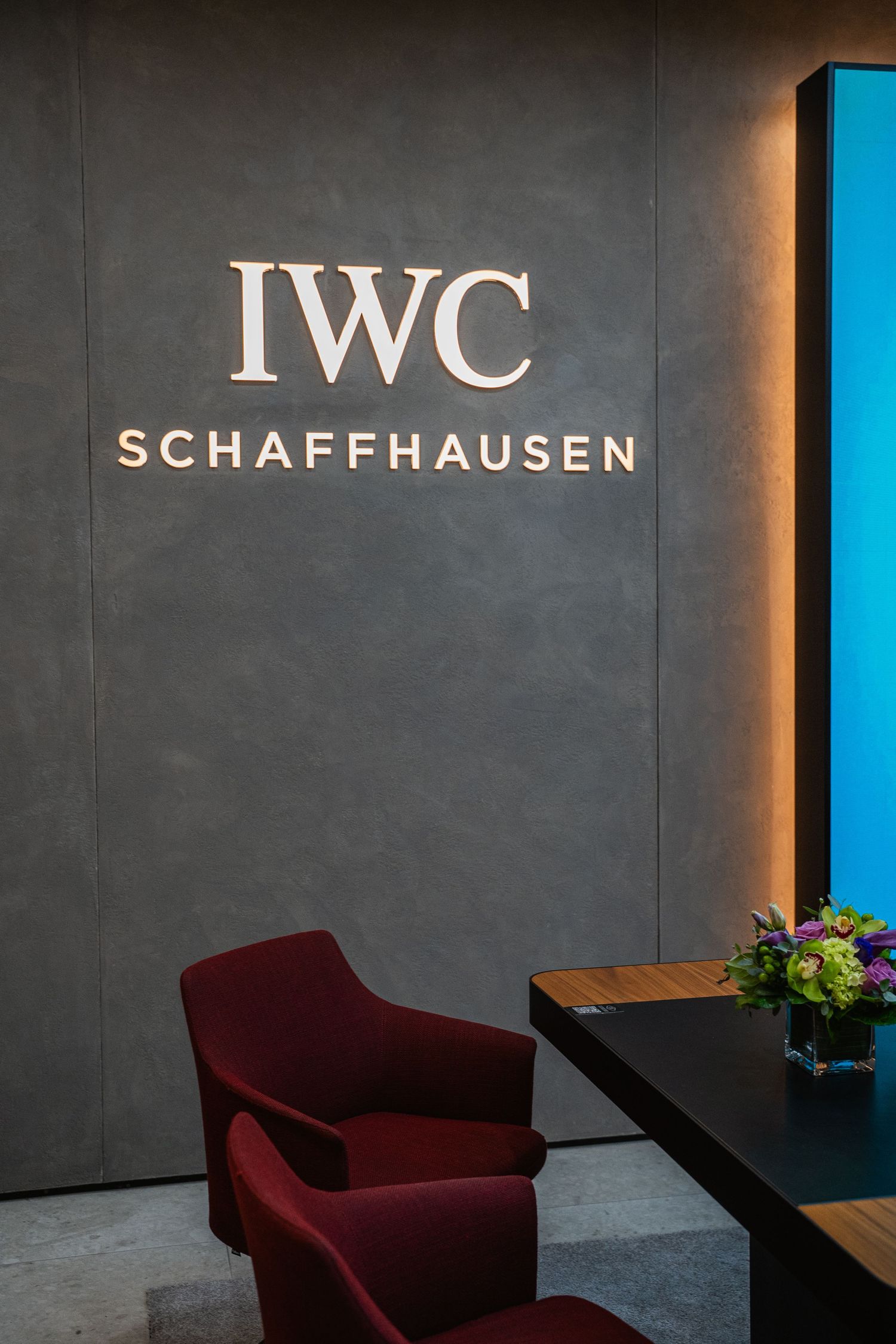 IWC Schaffhausen luxury watch brand logo displayed on a sleek grey wall with burgundy seating.
