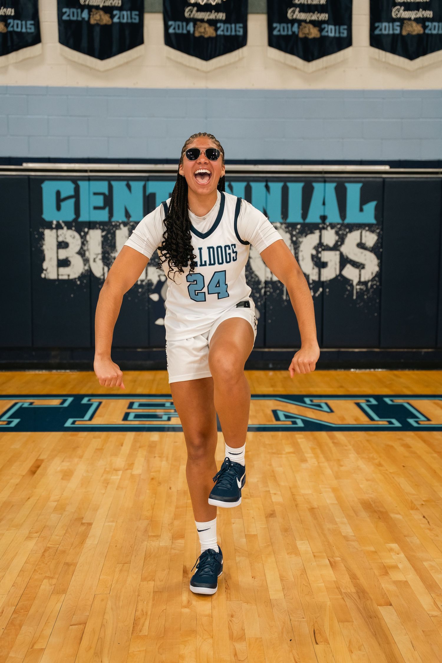 Energetic basketball player in white Bulldogs jersey number 44 posing on court with championship banners.