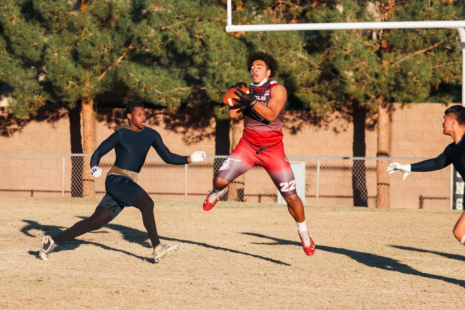 Athletes compete during intense flag football play with player jumping to catch ball.