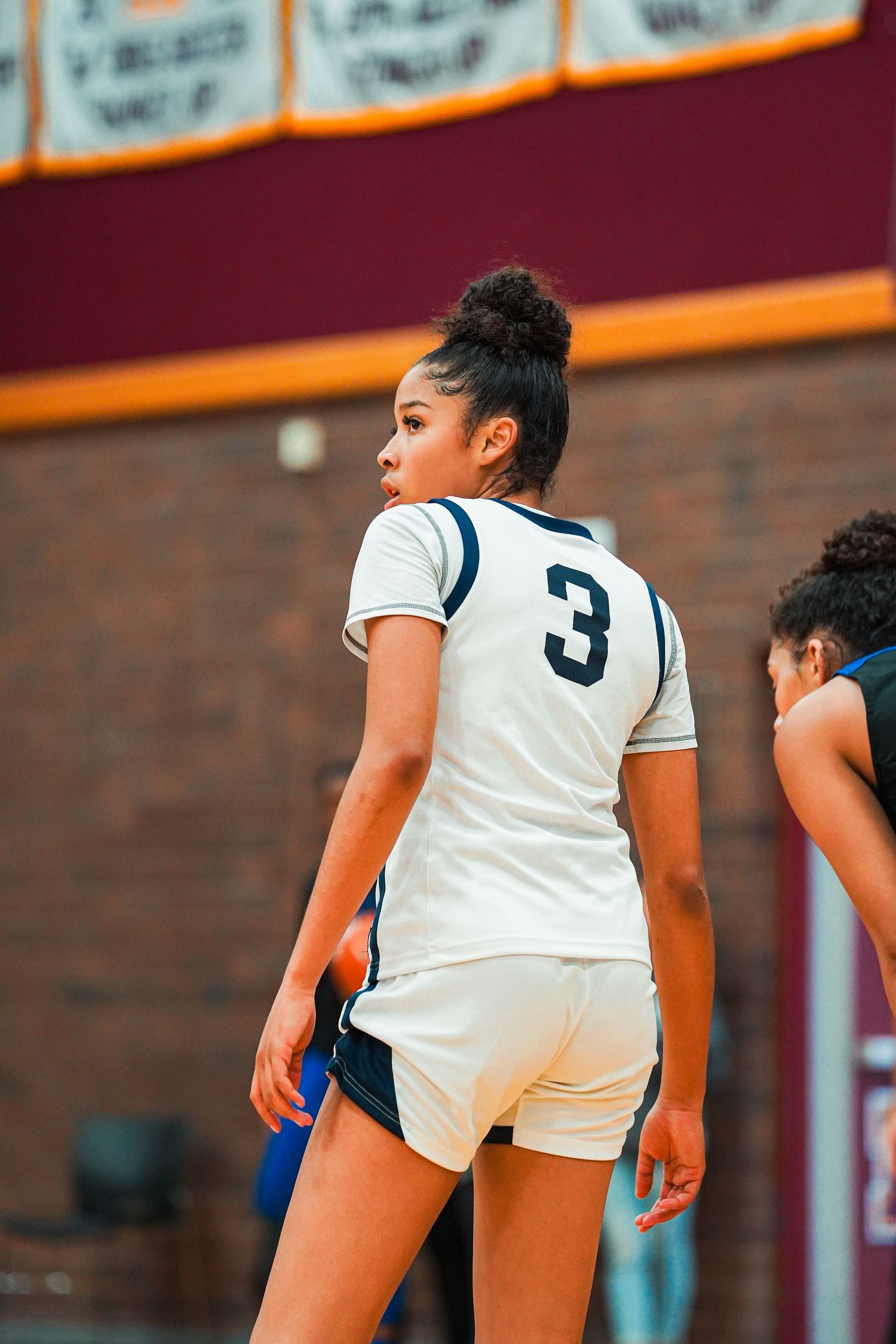 Basketball players in white jerseys demonstrate defensive positions during practice.