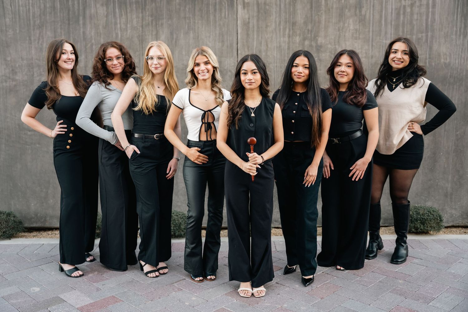 A group of women posing together in coordinated black and neutral outfits.
