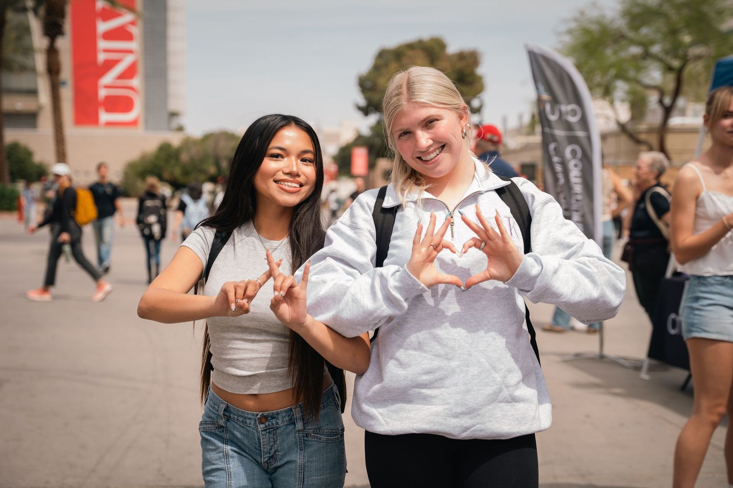 Two students make heart shapes with their hands while posing at a campus event.