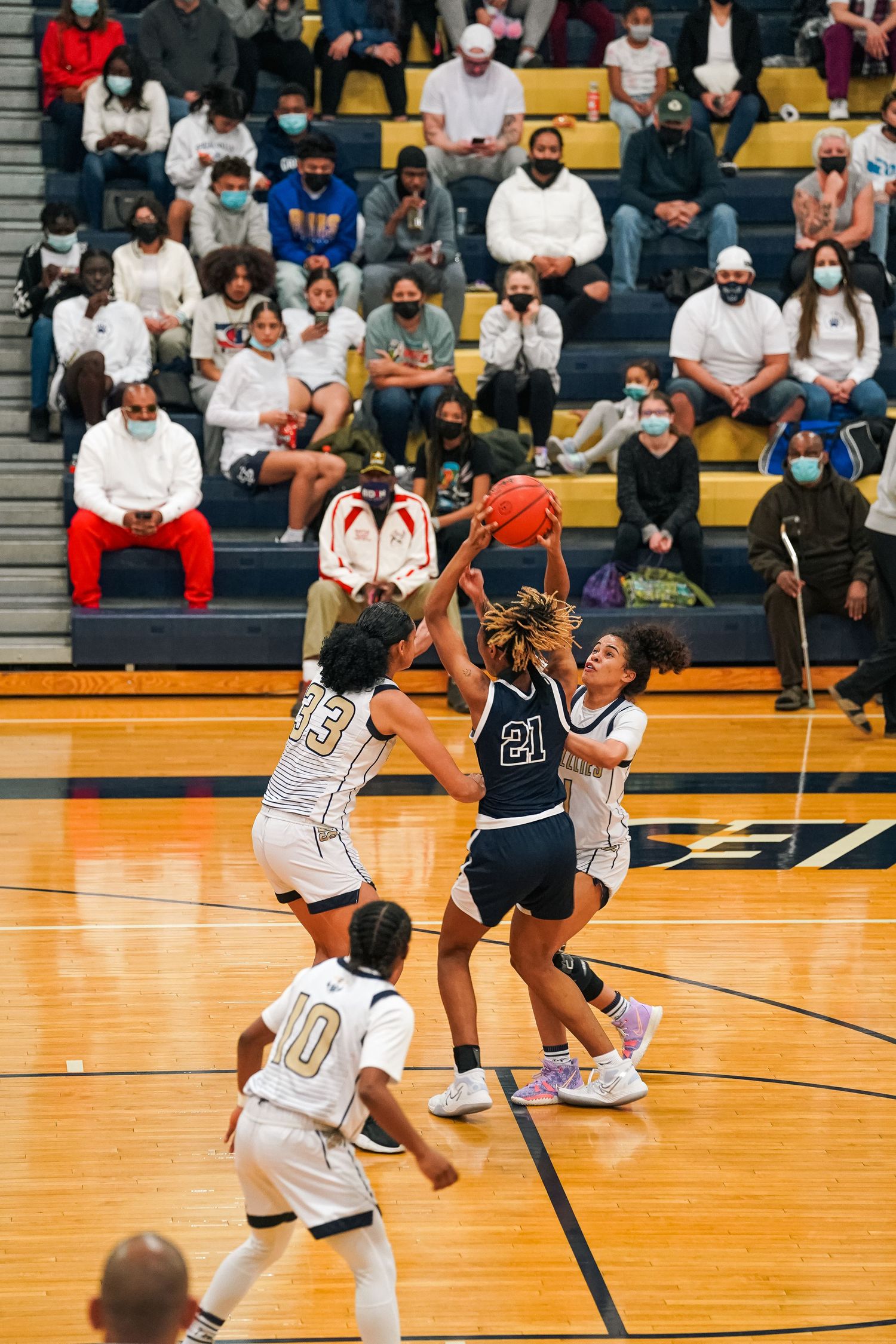 Basketball players compete for possession during an intense game on a brightly lit indoor court.