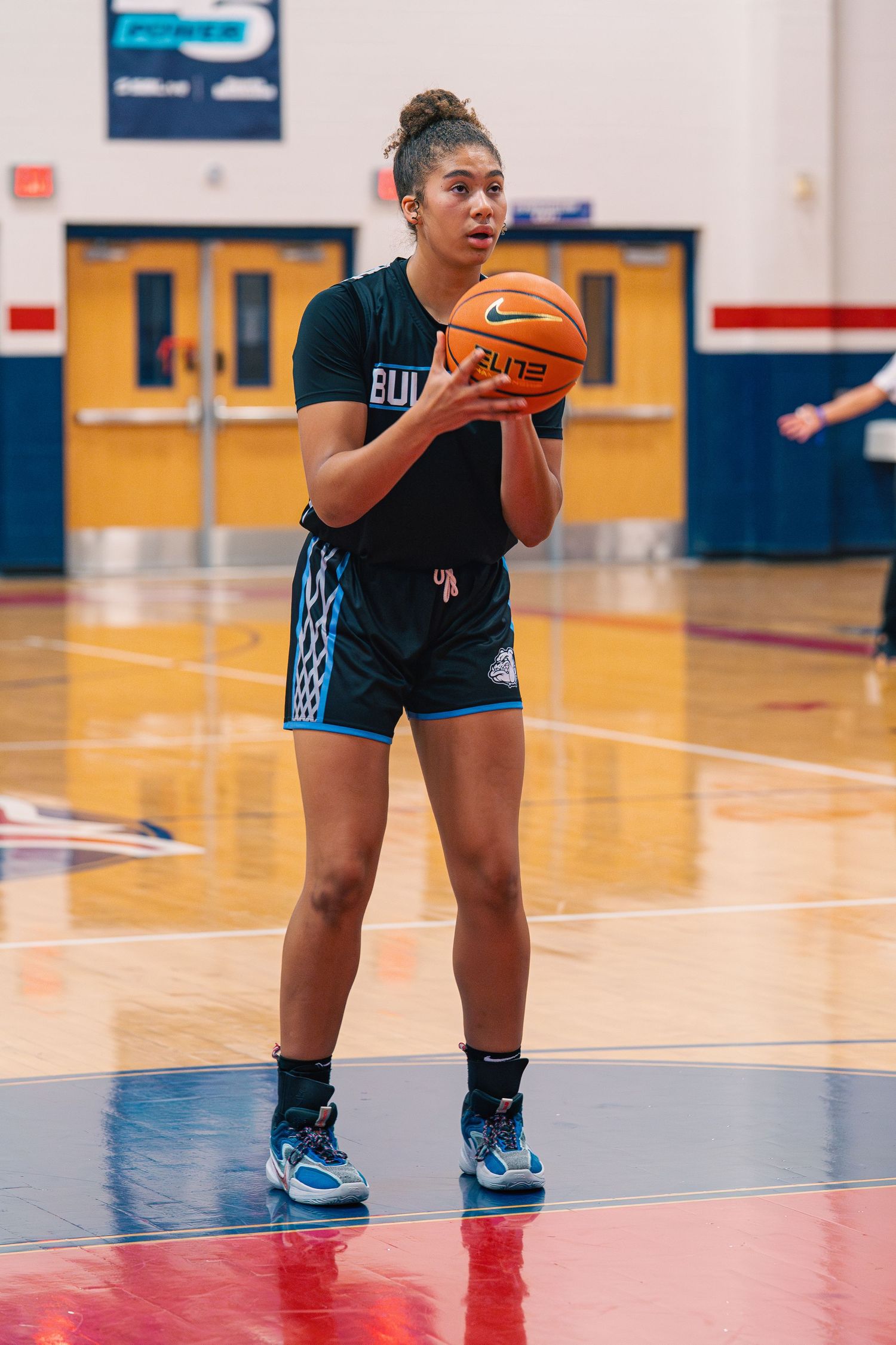Basketball player in a black uniform with knee pads dribbles on a gymnasium court.