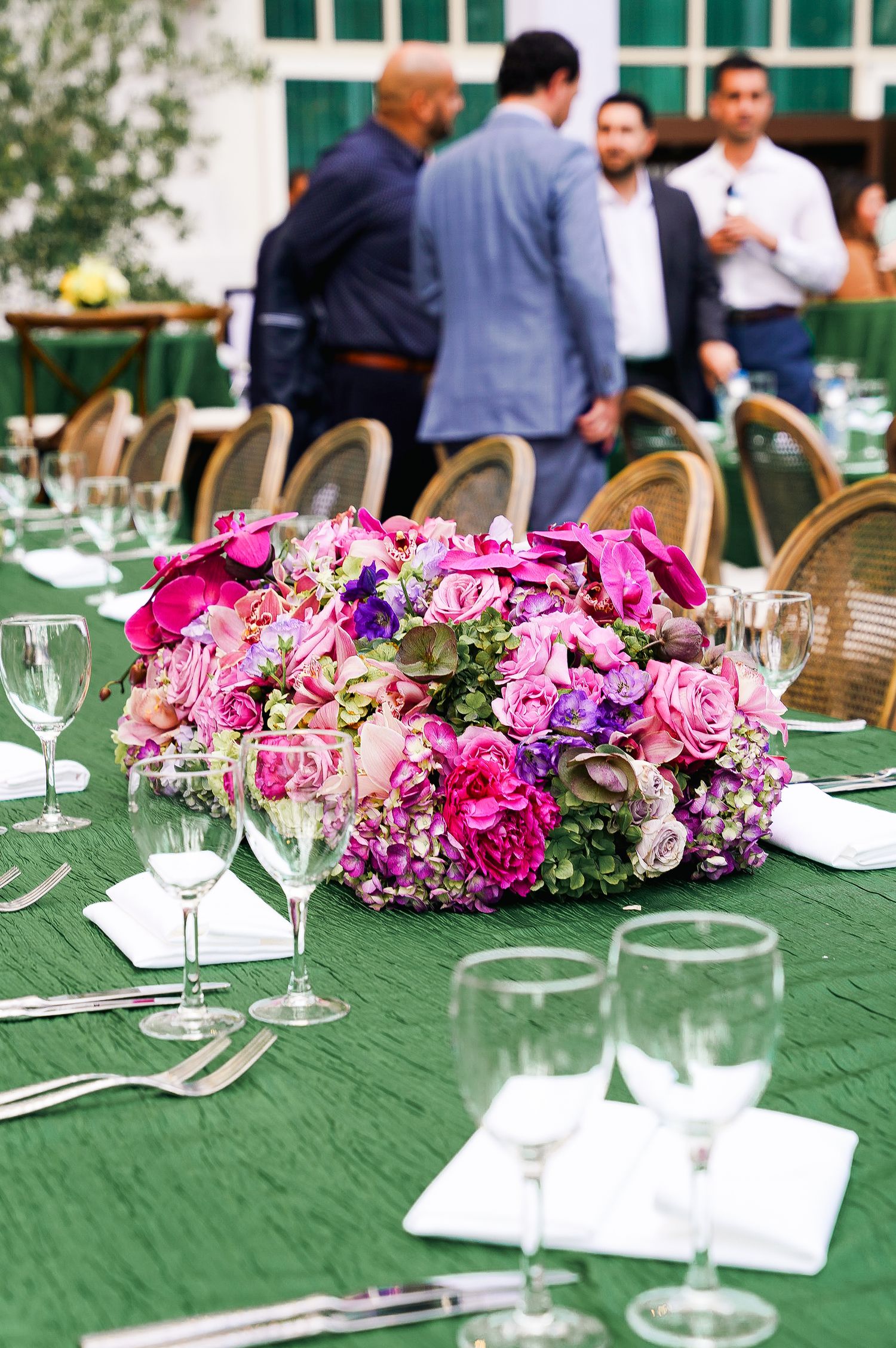 Vibrant pink and purple floral arrangements decorating elegant table settings with wine glasses.