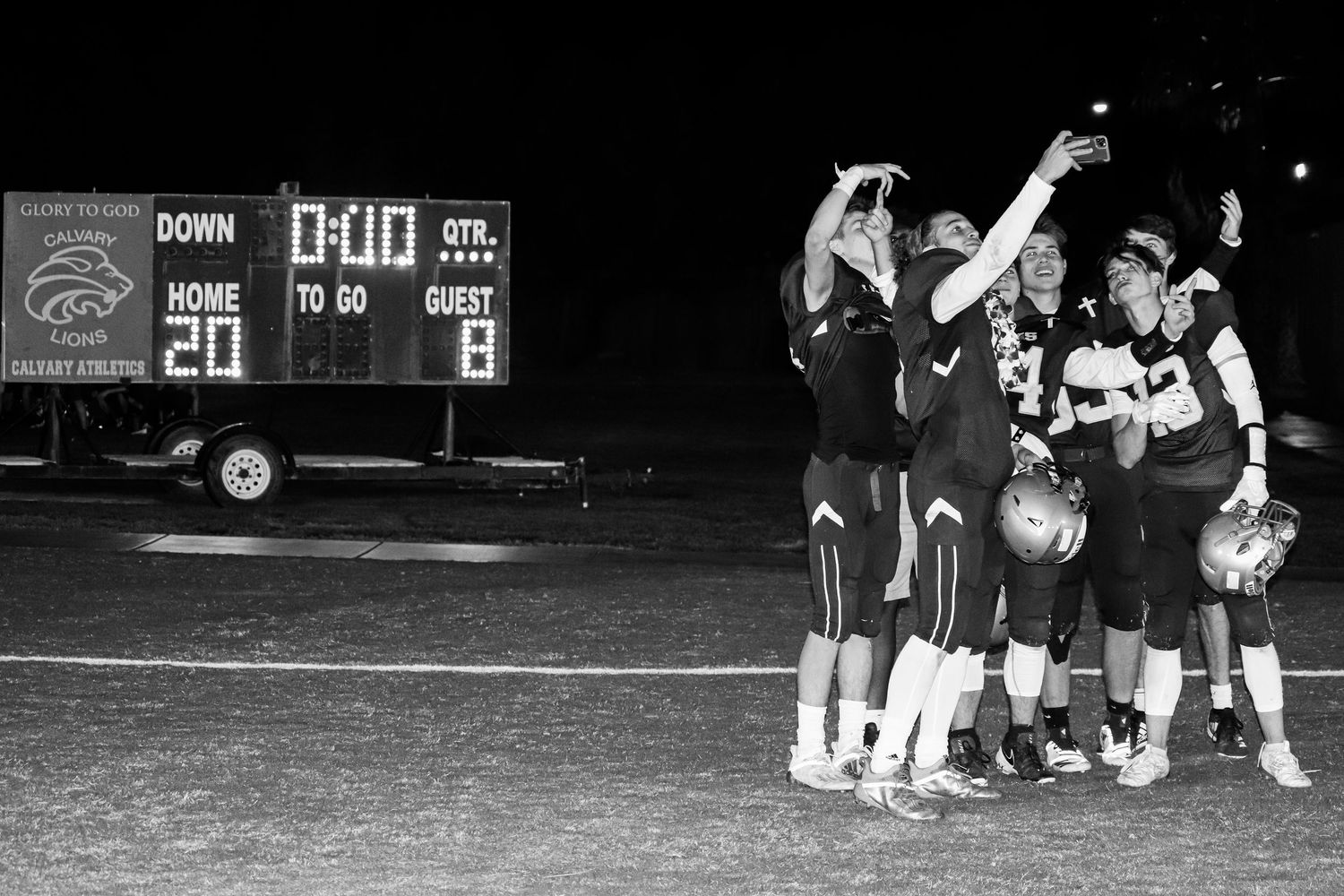 Sports team celebrates victory under night lights with scoreboard in background.