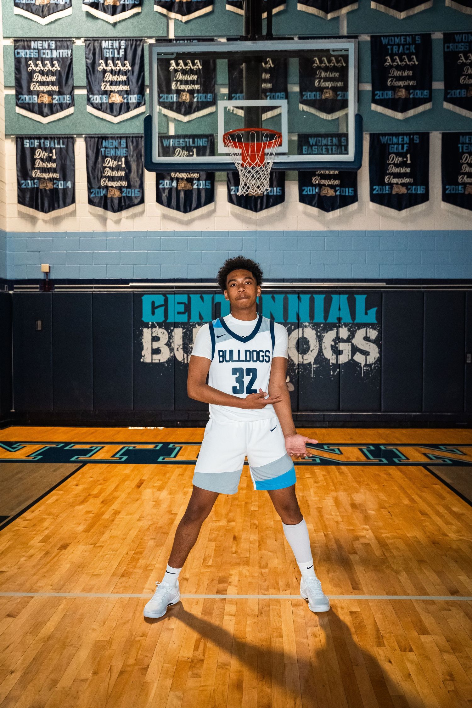 Basketball player in white Bulldogs jersey number 32 poses on court under championship banners.