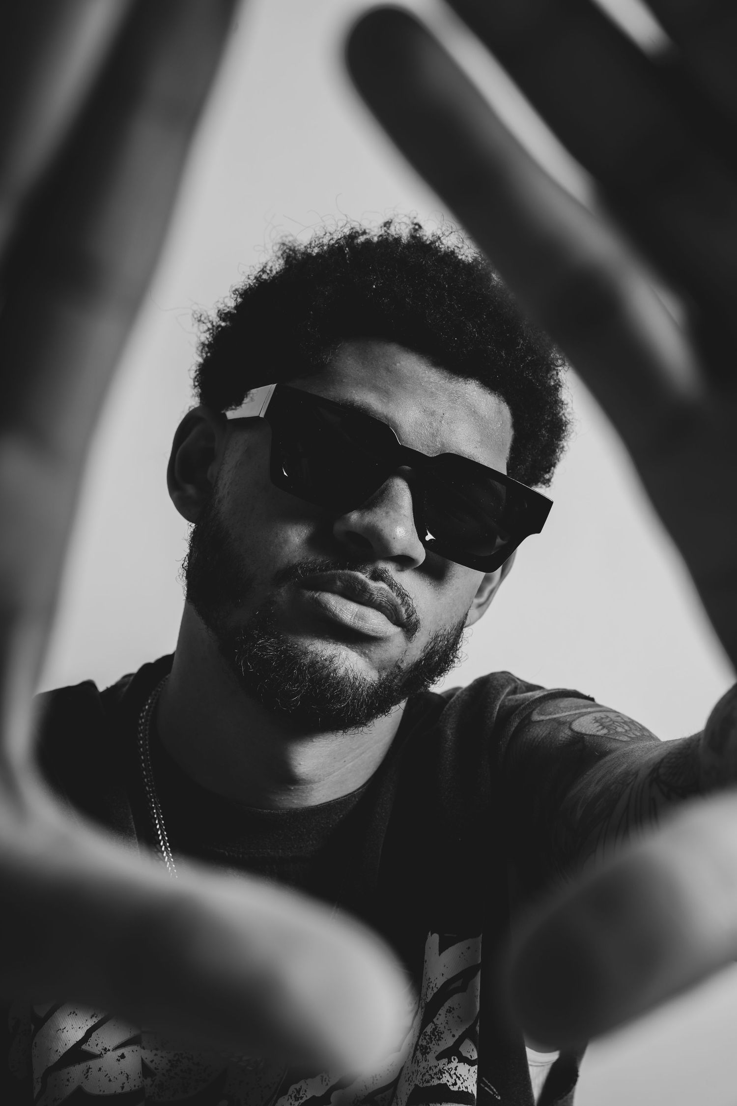 Monaco Media. Dramatic black and white portrait shot through foreground elements of person wearing sunglasses.
