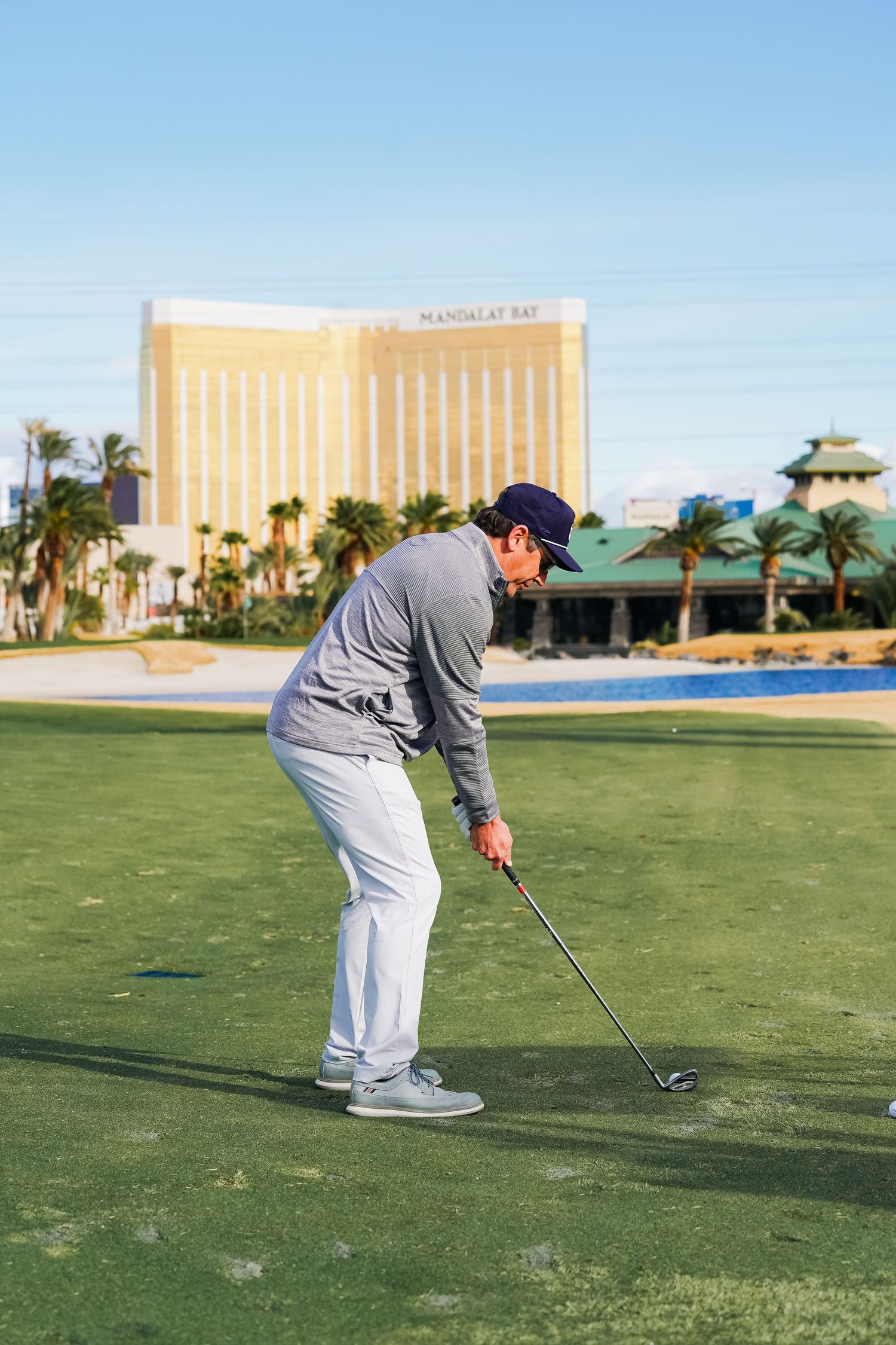 Golfer takes a putt on a Las Vegas golf course with the Mandalay Bay hotel visible in the background.