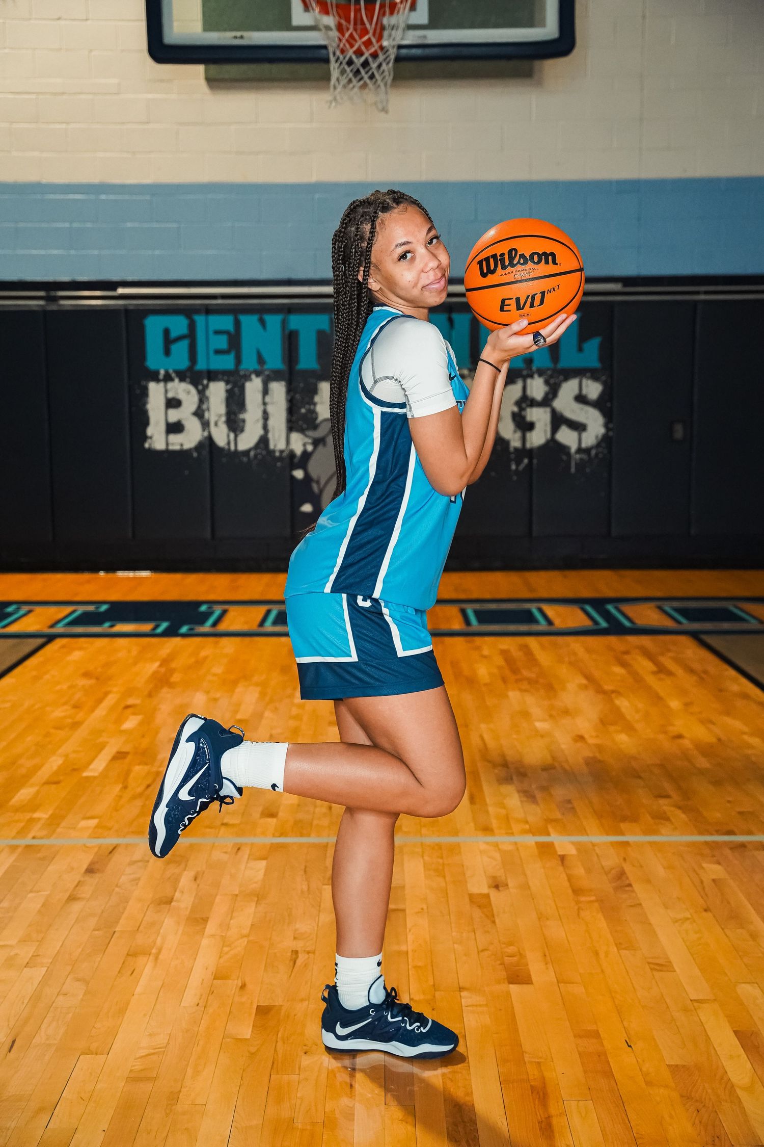 Basketball player in turquoise uniform practices shooting form with Wilson ball in gymnasium.