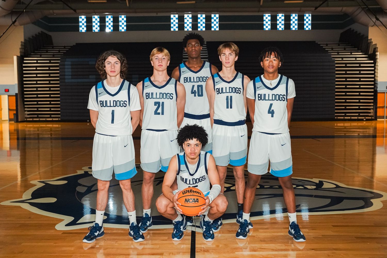 Six basketball players in white Centennial Bulldogs uniforms pose together on their home court.