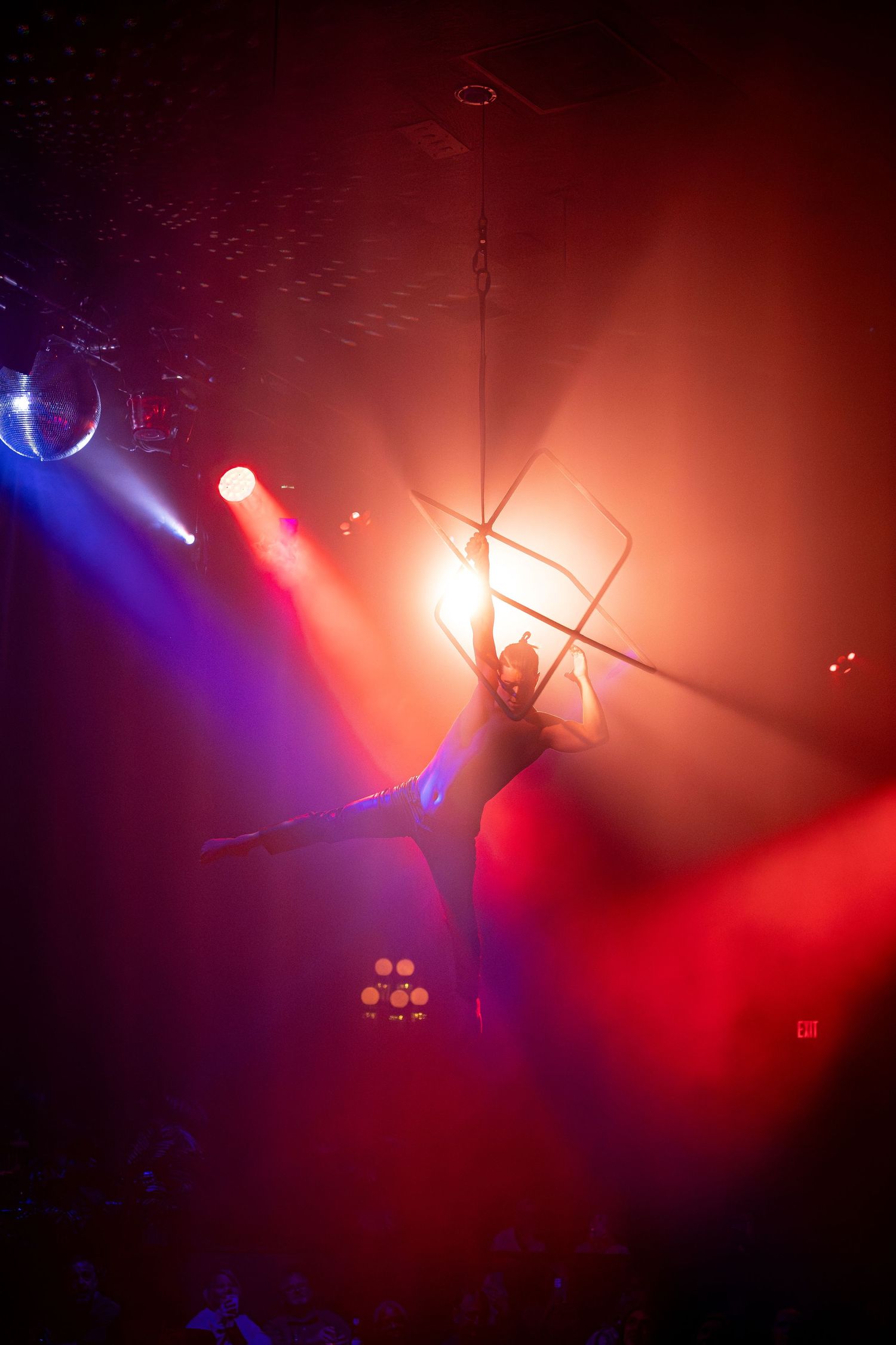 Aerial performer suspended in dramatic pose with red and blue theatrical lighting.