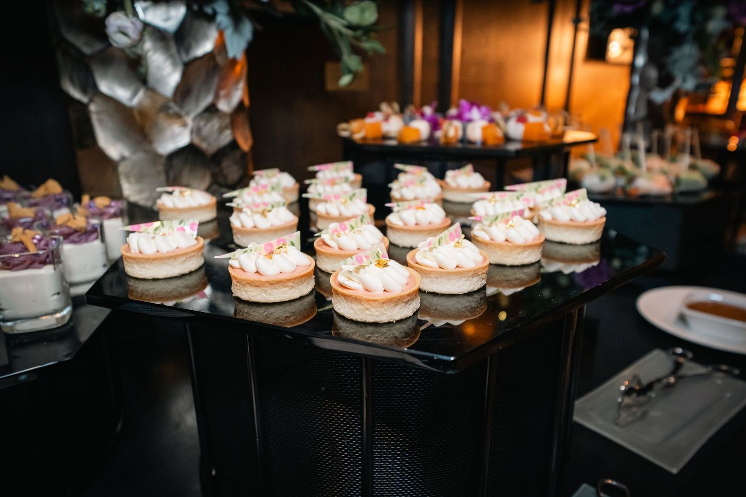 Delicate cream-filled pastries topped with frosting displayed on tiered black platforms.