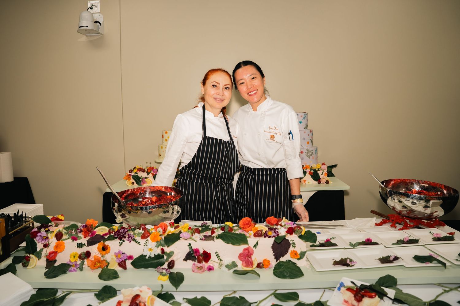 Two chefs in professional attire stand behind catering display of fresh vegetables.