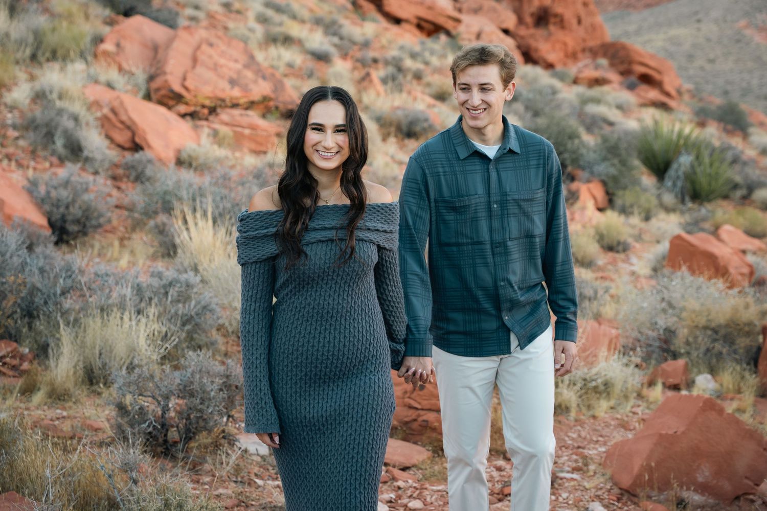 A couple in coordinating blue outfits holding hands while walking through a red rock desert landscape.