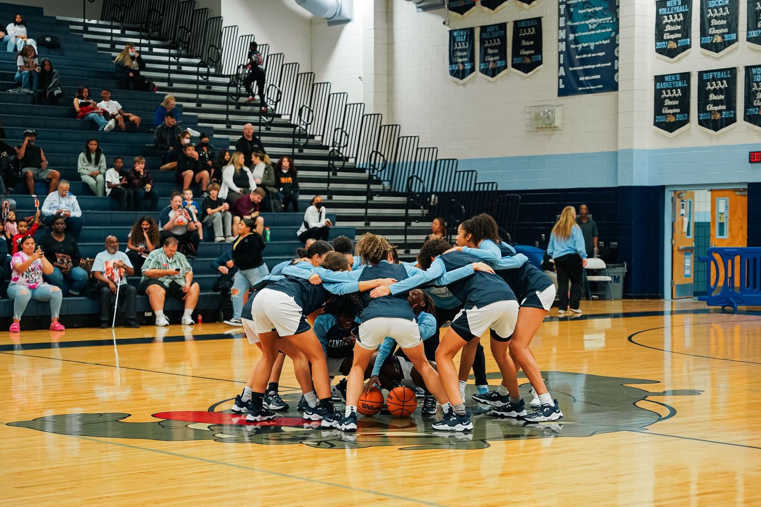 Wide view of a basketball game in progress with spectators in the bleachers.