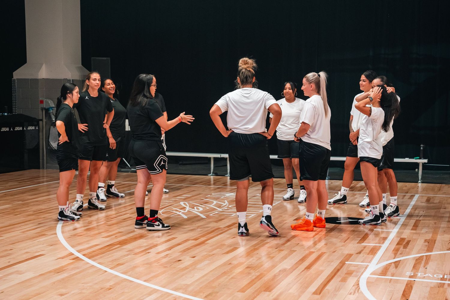 Group of athletes in practice uniforms gathered on basketball court during training session.