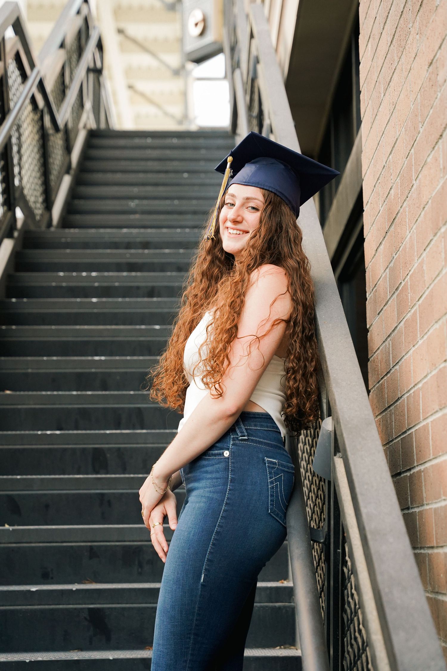 Graduate in cap and gown poses on industrial staircase.
