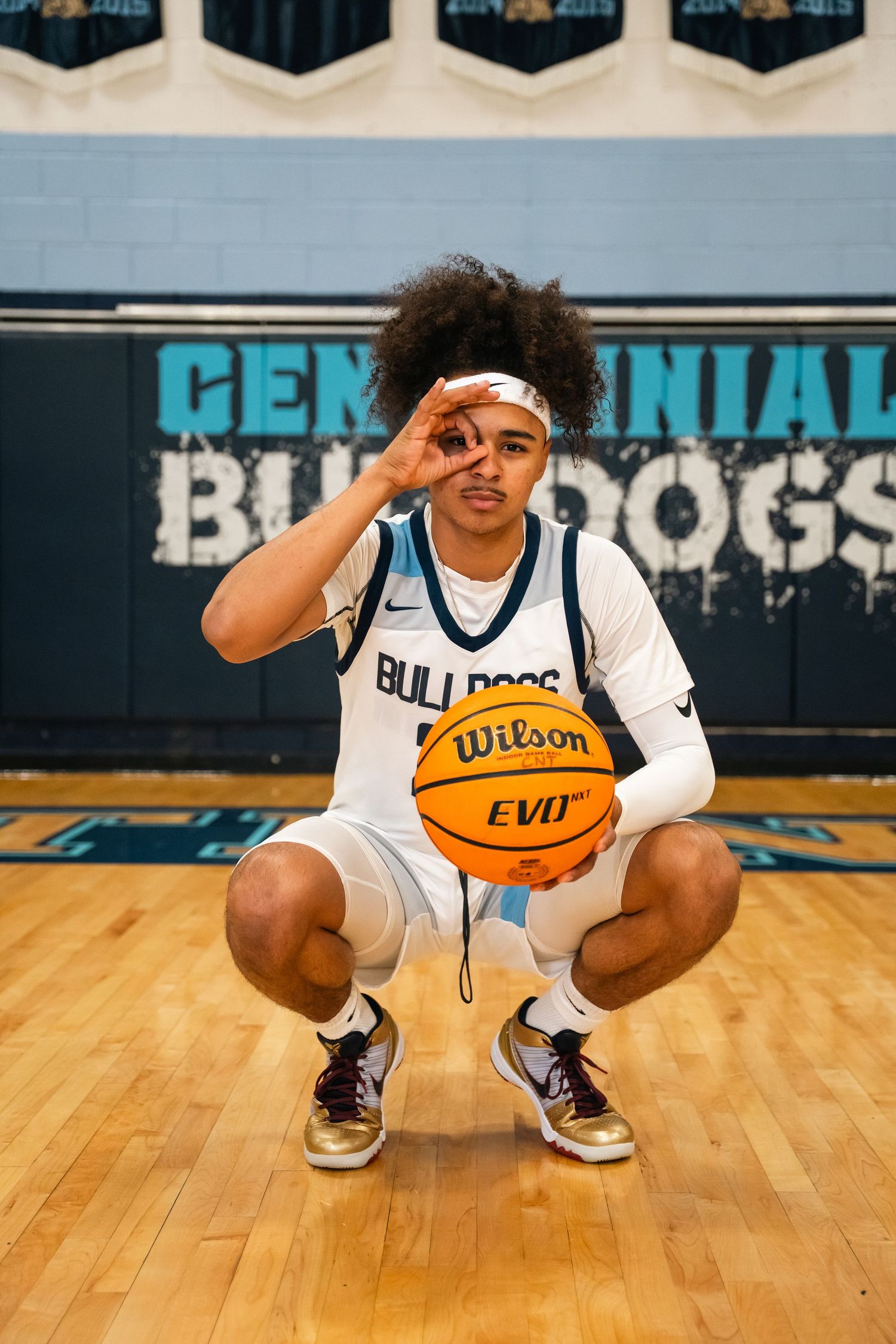 Basketball player crouching on court holding Wilson basketball in white Bulldogs uniform.