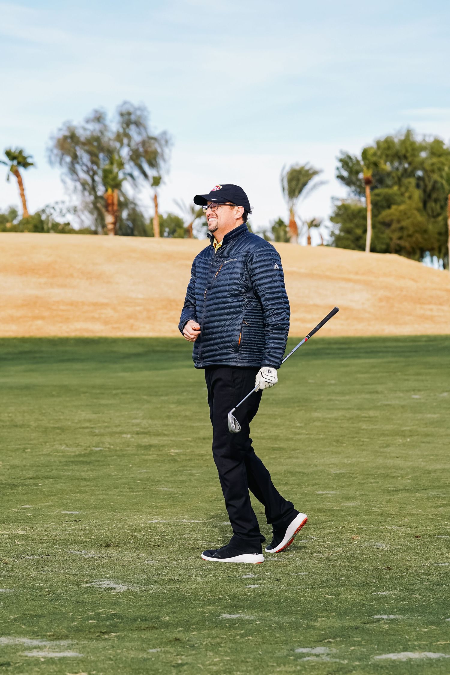 Golfer walking across the fairway carrying a golf club at a desert golf course.