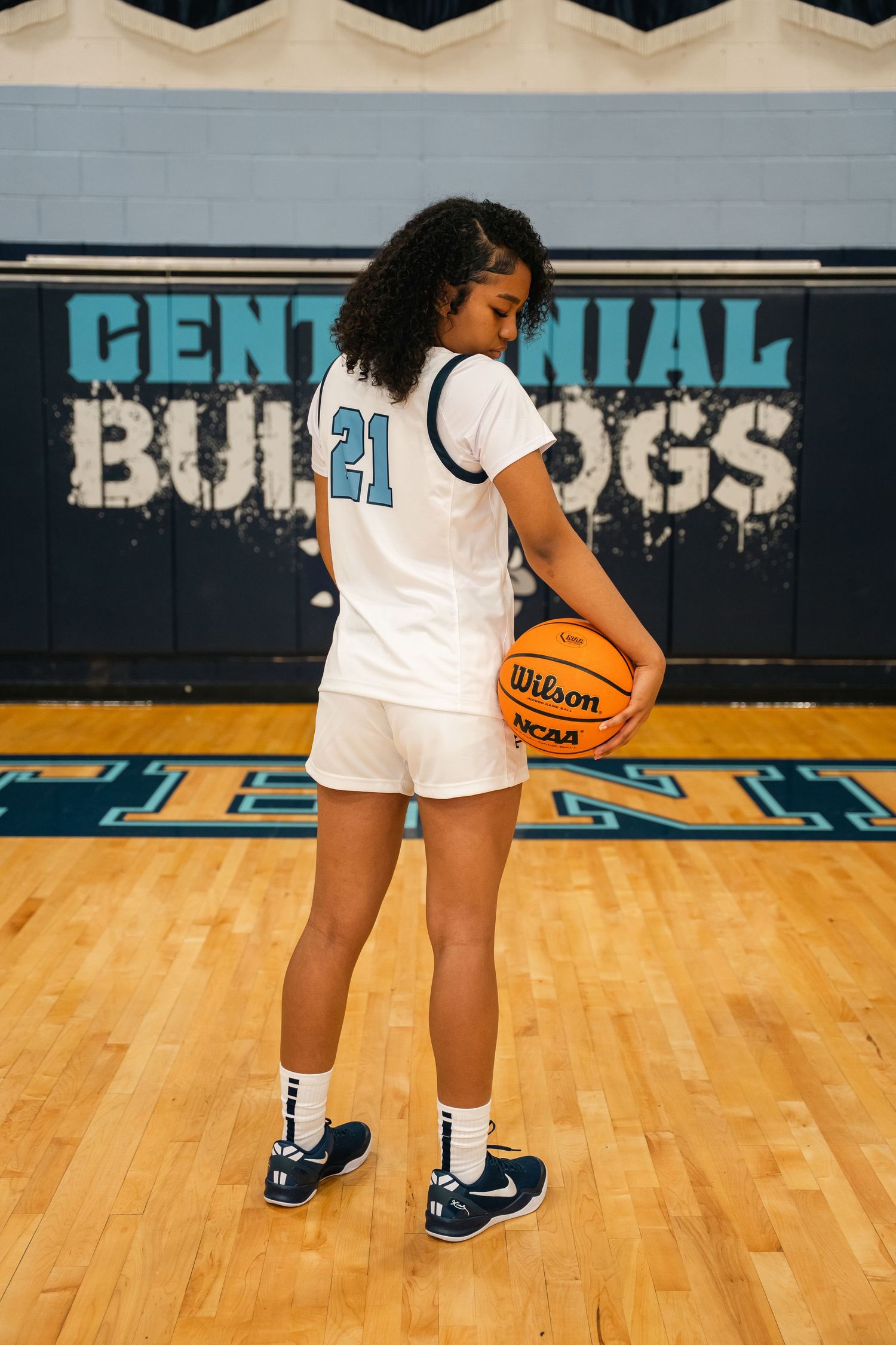 Close-up of basketball shoes and uniform shorts on wooden gym floor.