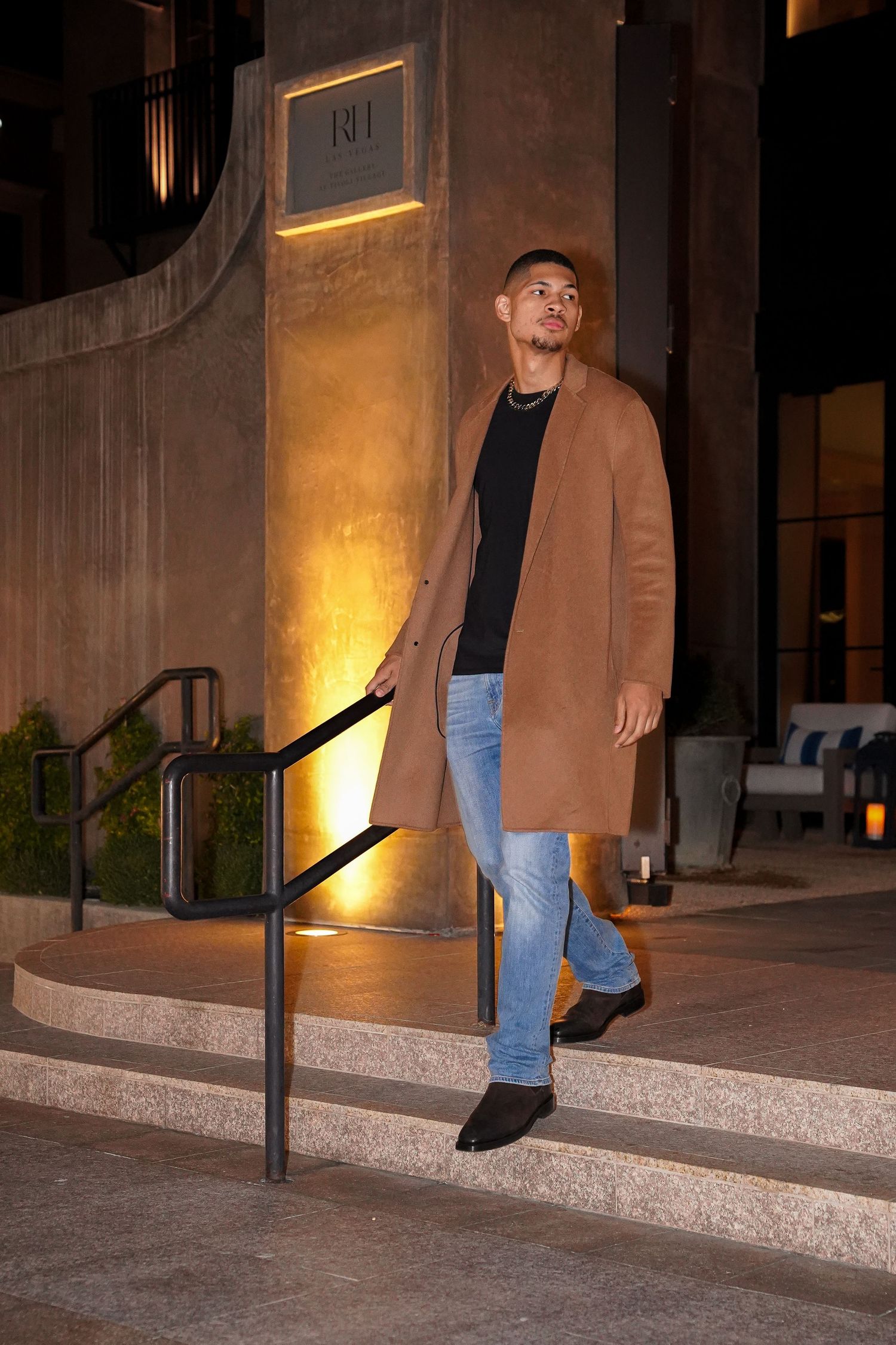 Person in tan overcoat demonstrating walking poses on concrete steps at night.