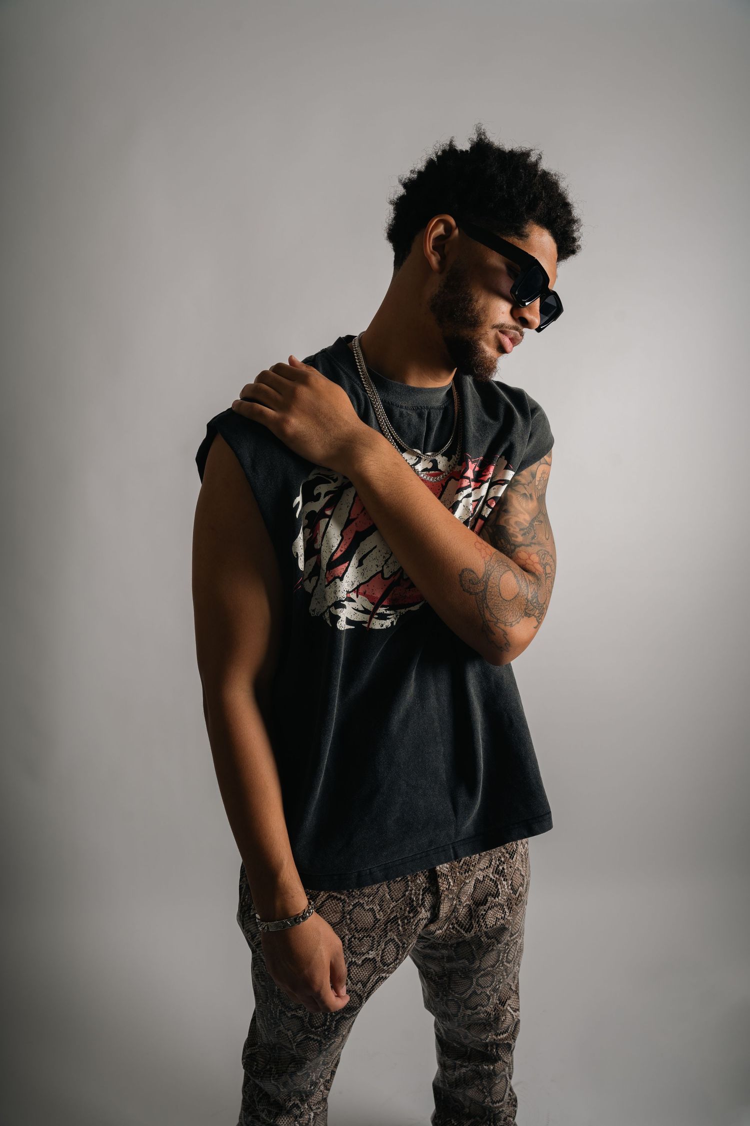 Candid studio fashion shot showing casual pose in sleeveless graphic tee and patterned pants.