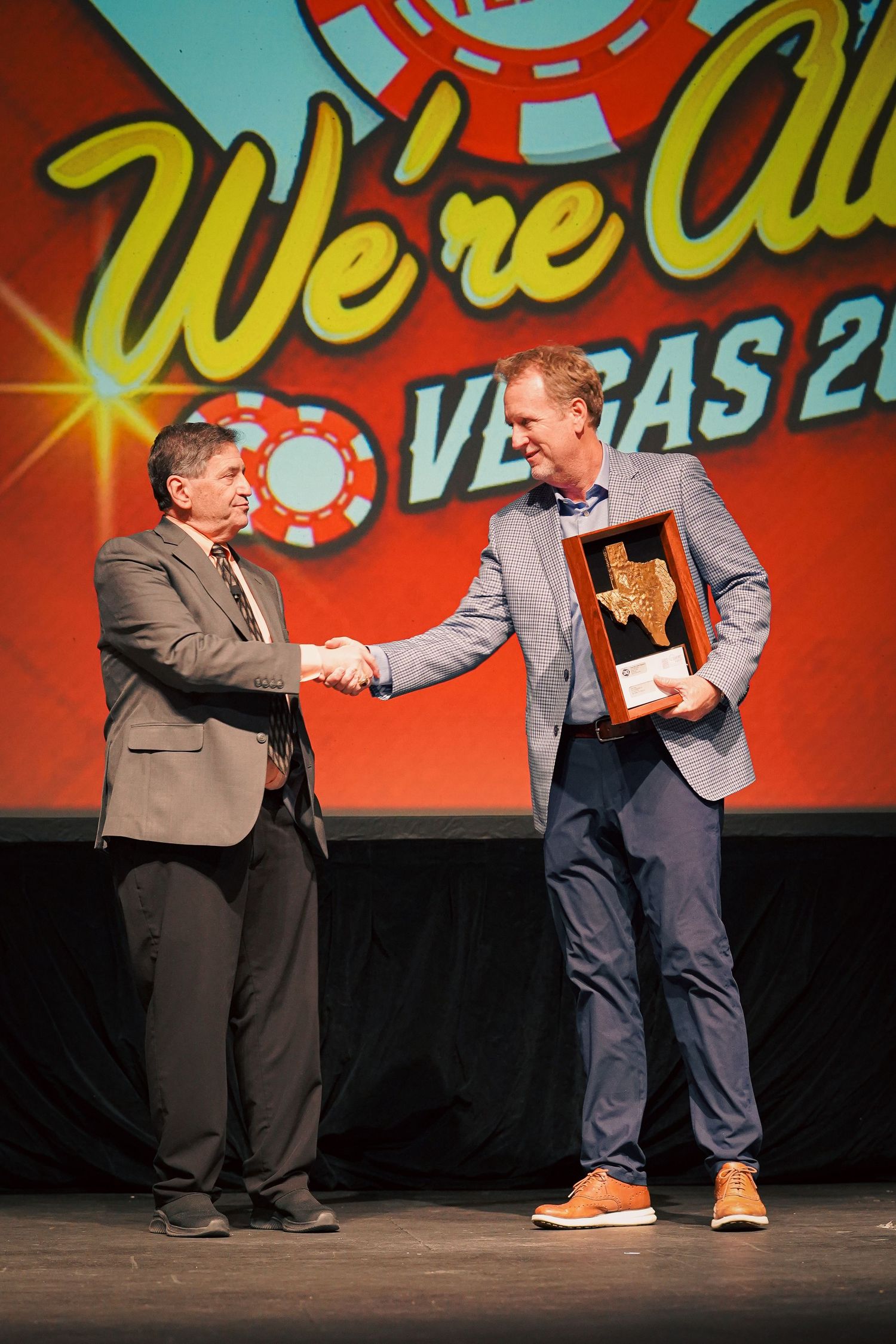Business professionals shake hands during award ceremony with Vegas signage.