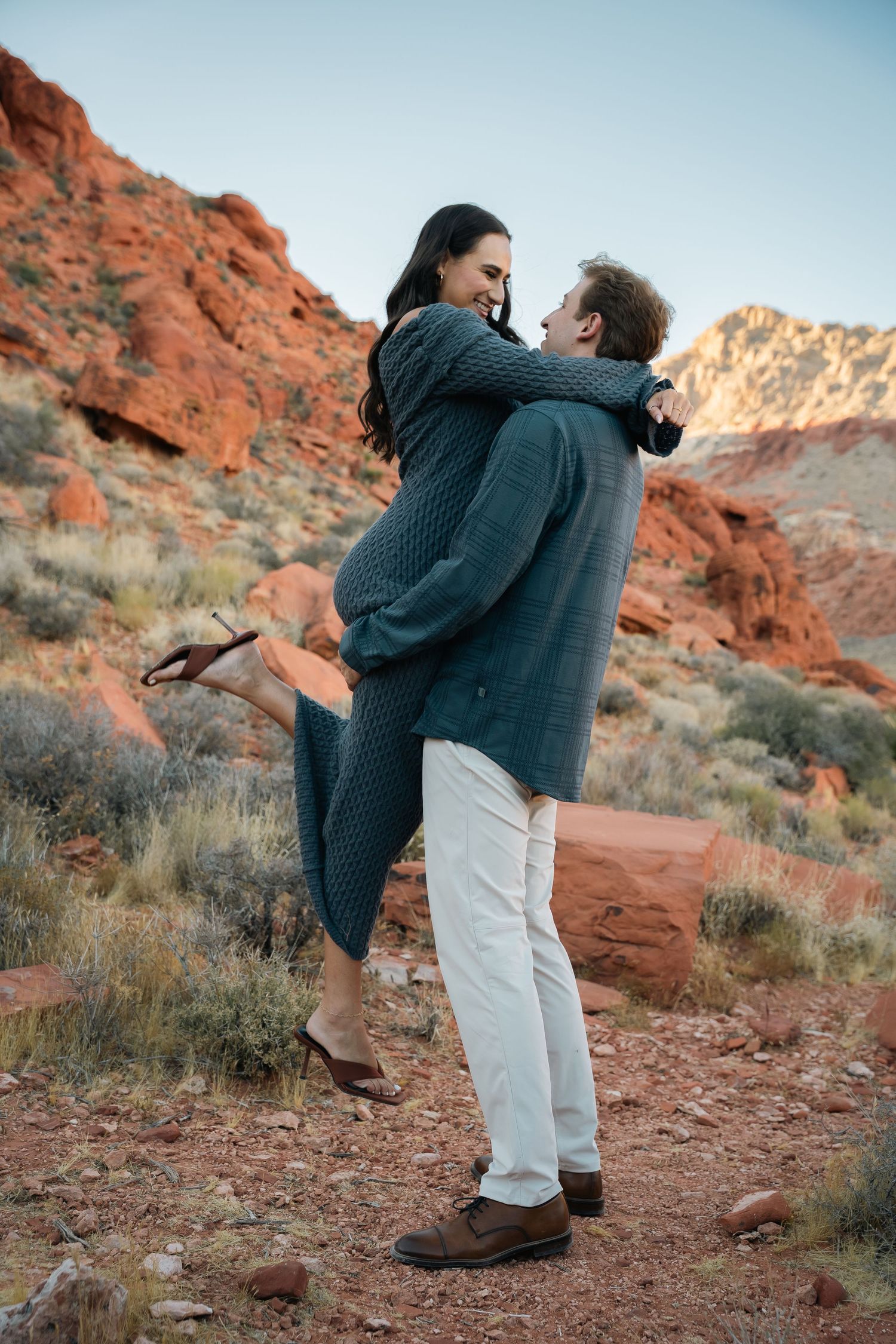 A romantic lift pose between a couple surrounded by red rock cliffs at dusk.