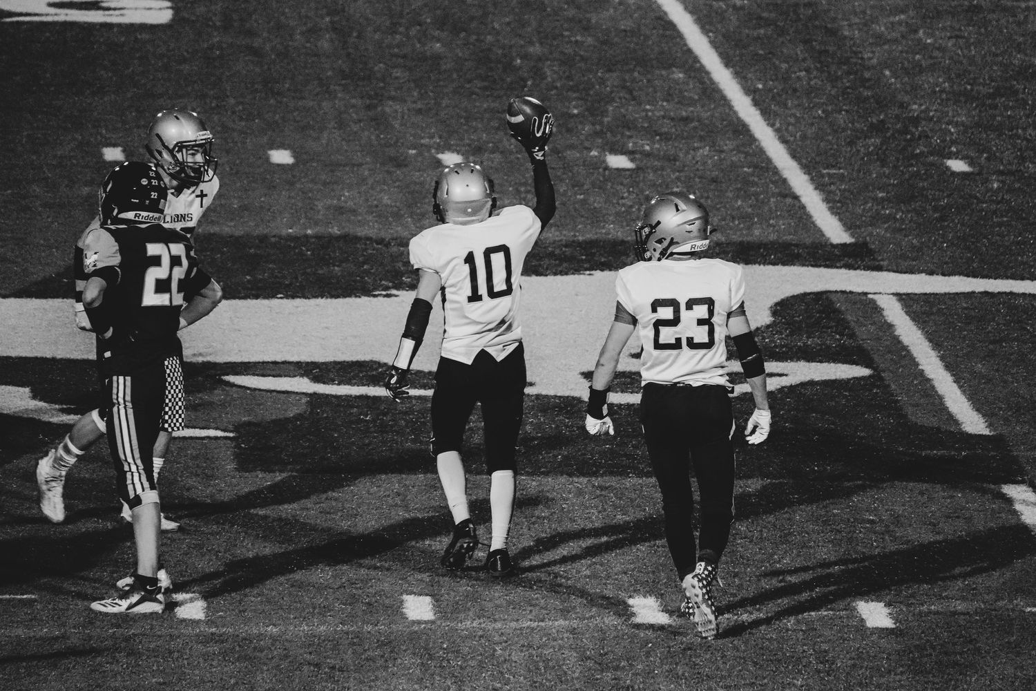 Three football players on field with referee during black and white game action.