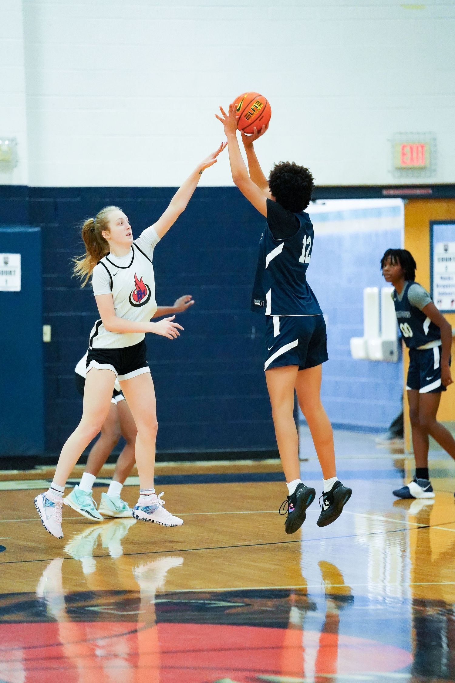 Two players jump for basketball during competitive game on indoor court.
