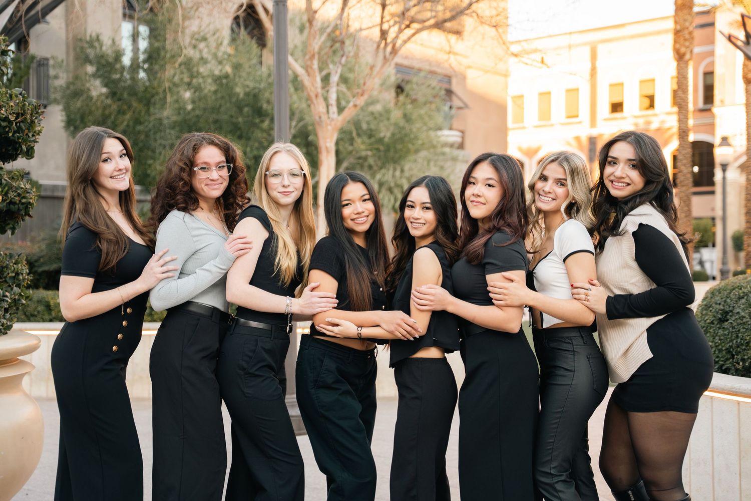 Group of friends in matching black outfits posing together outside a building at sunset.