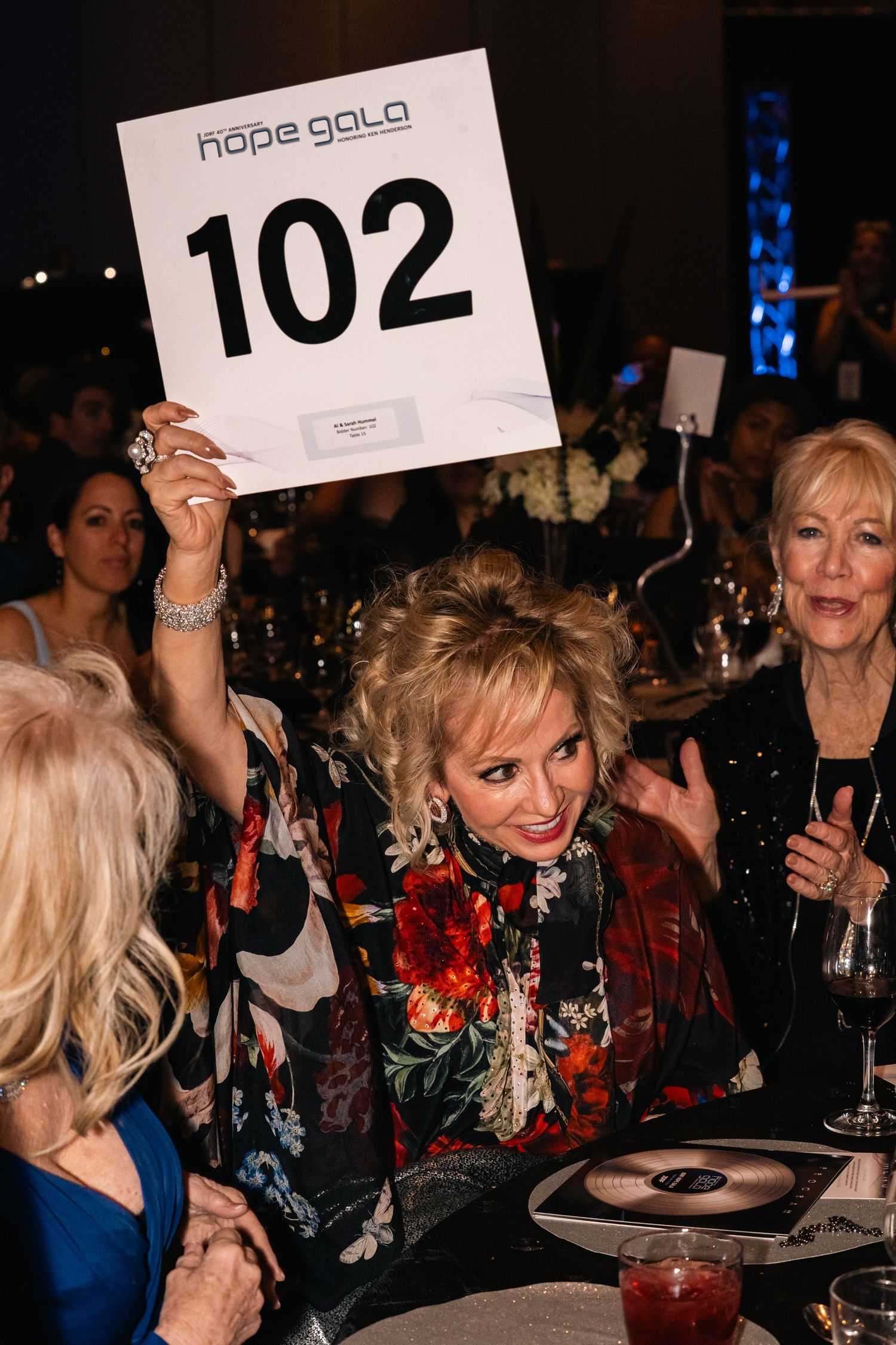 Excited attendees at Hope Gala holding up auction bidding paddle number 102.