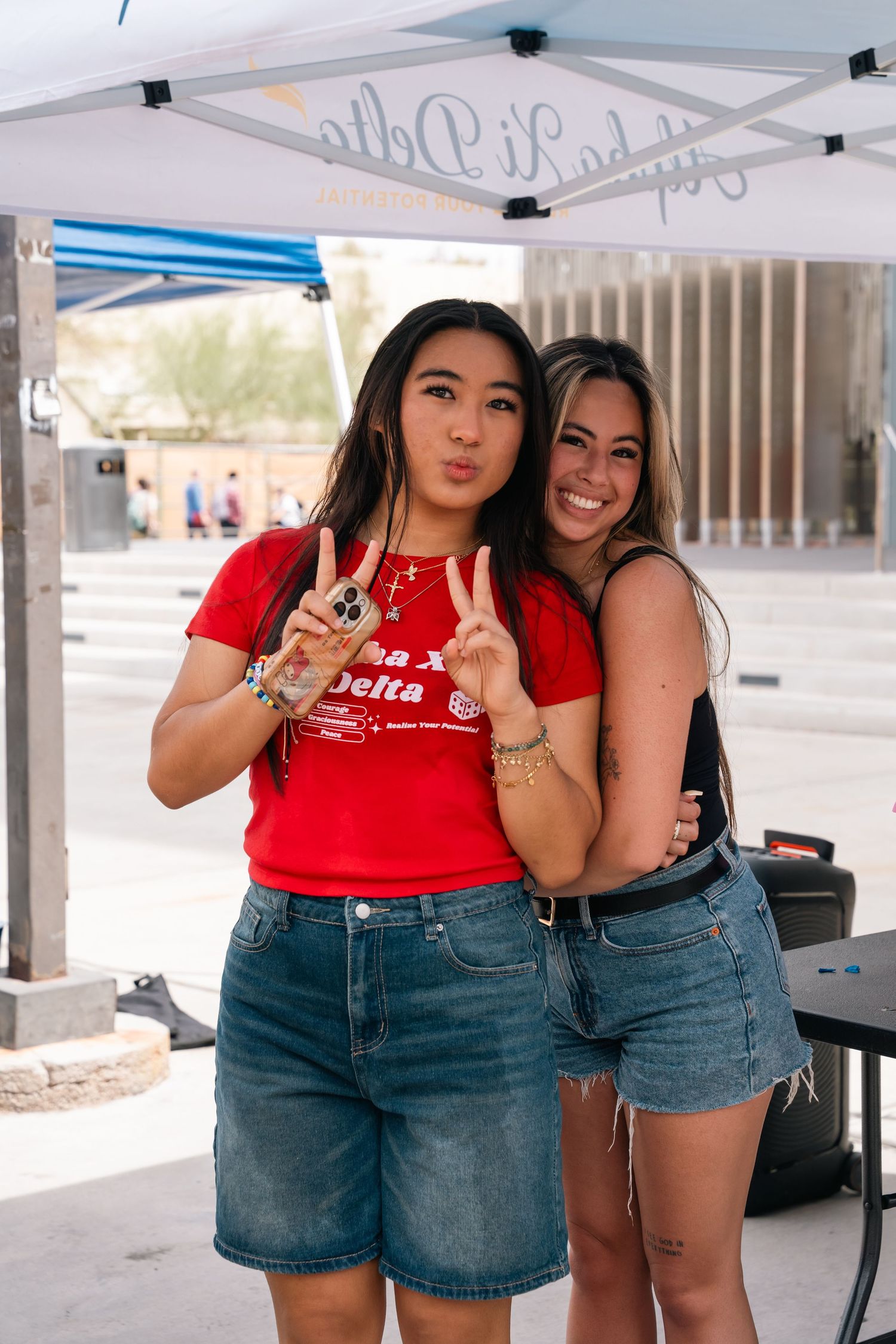 Two students posing together under white tent at campus event.