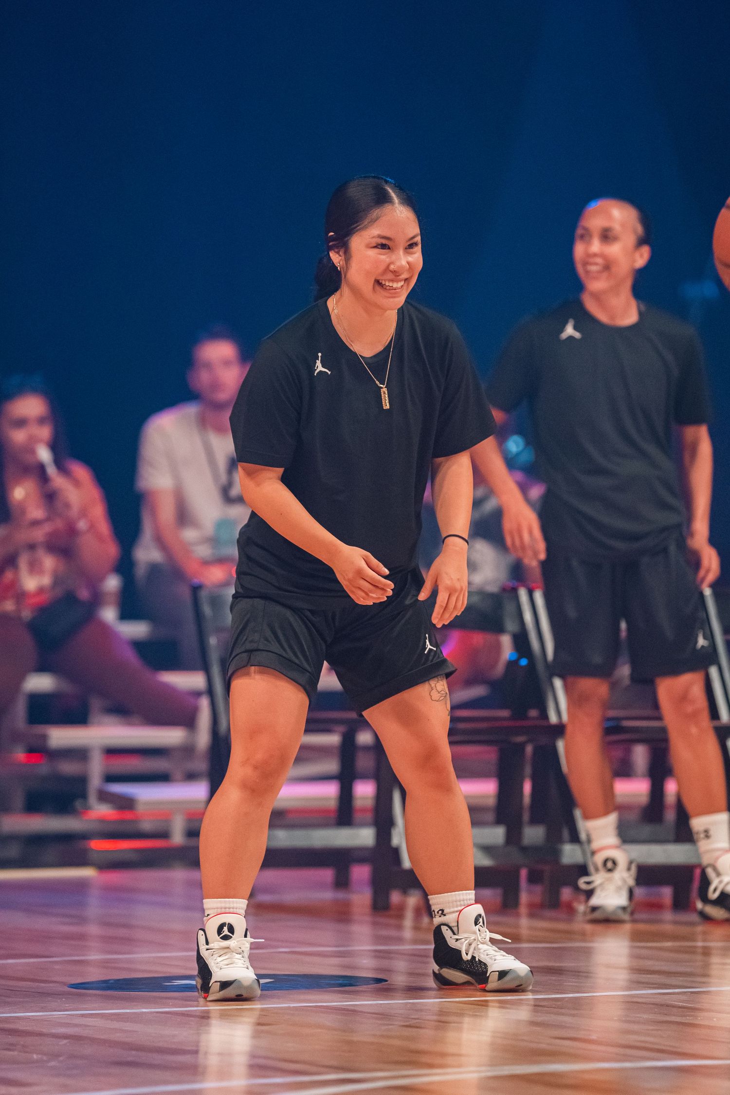 Athlete in black uniform smiling during basketball practice on indoor court.