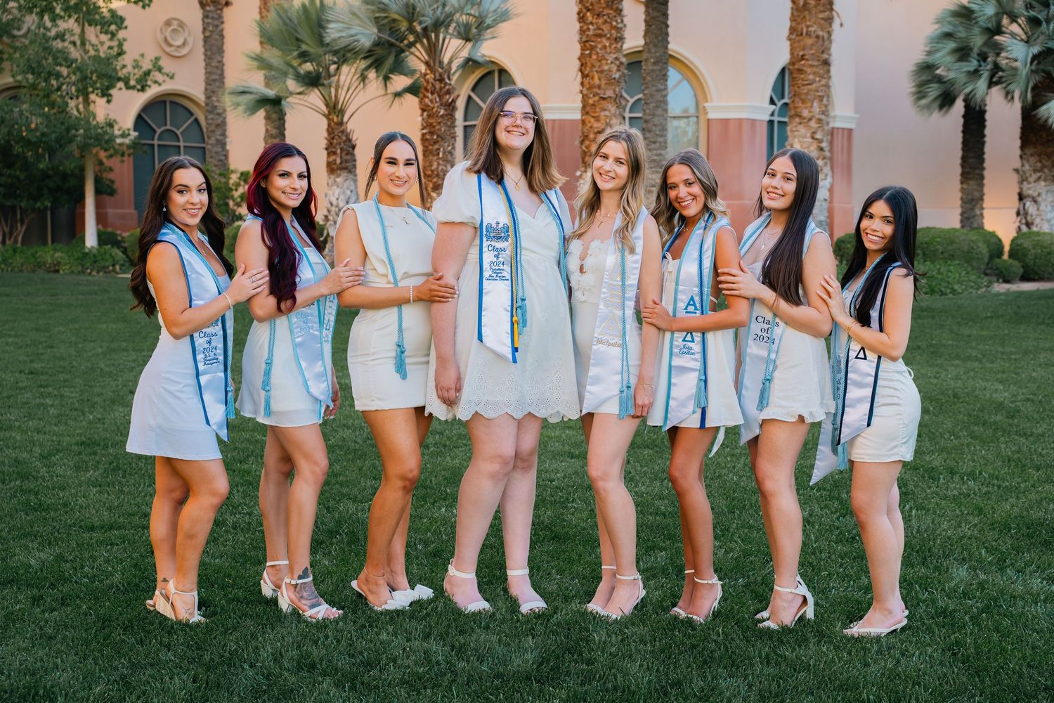Line of sorority members in white dresses and blue stoles pose for graduation photo.