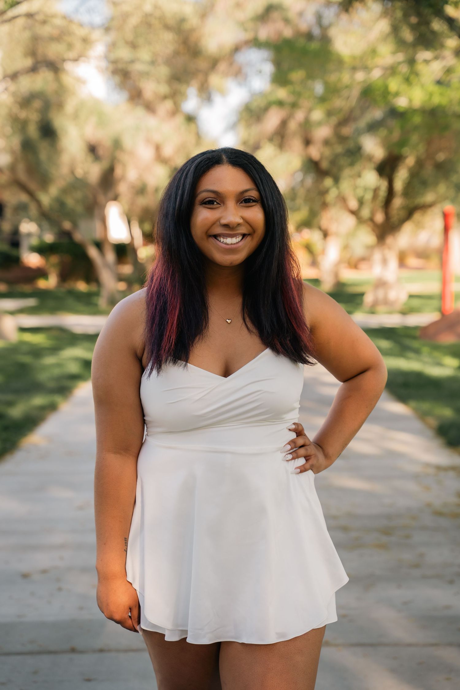 Woman in white sundress poses confidently on park pathway.