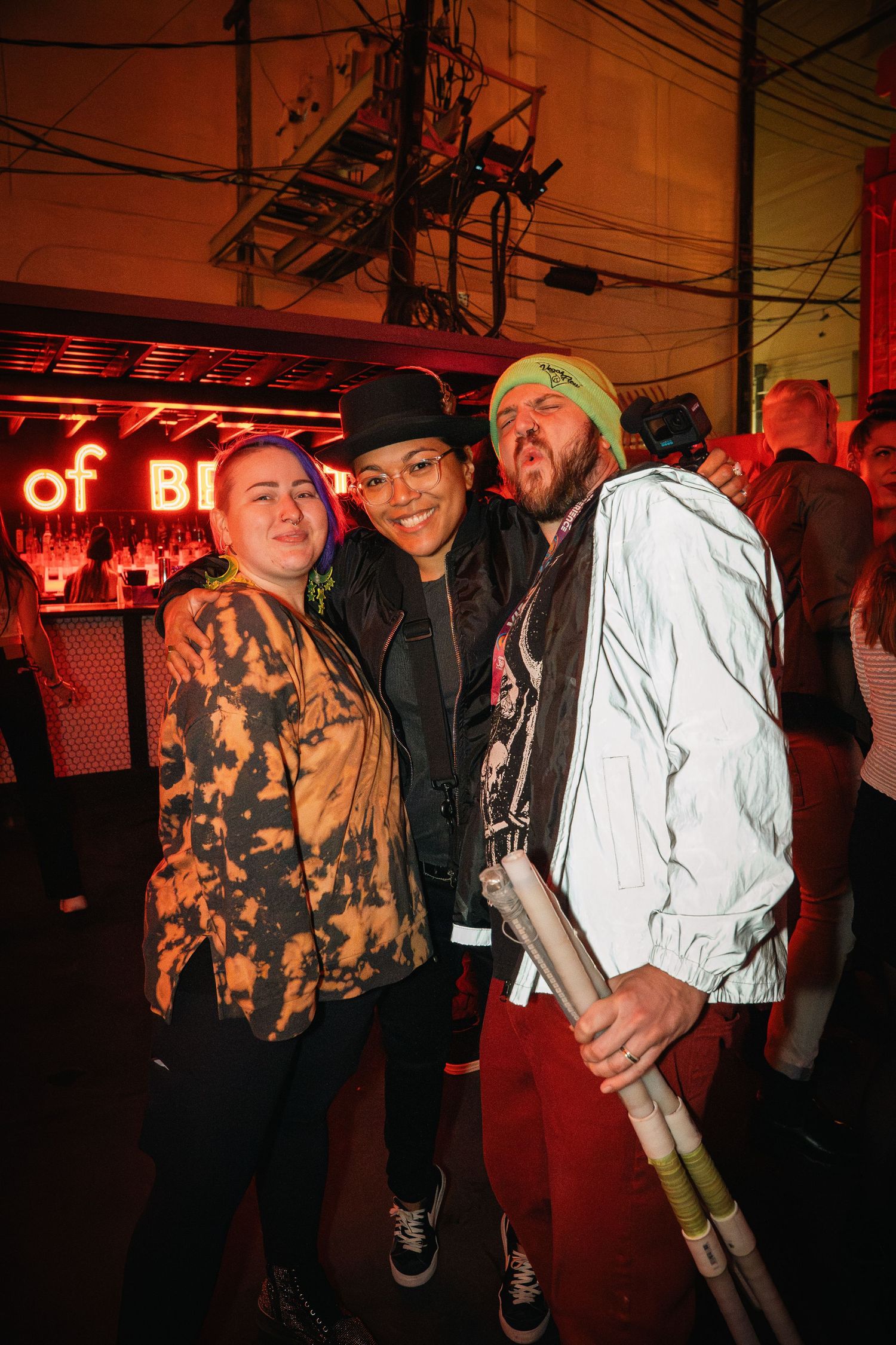 Three friends posing together at a nightclub under red neon lighting.