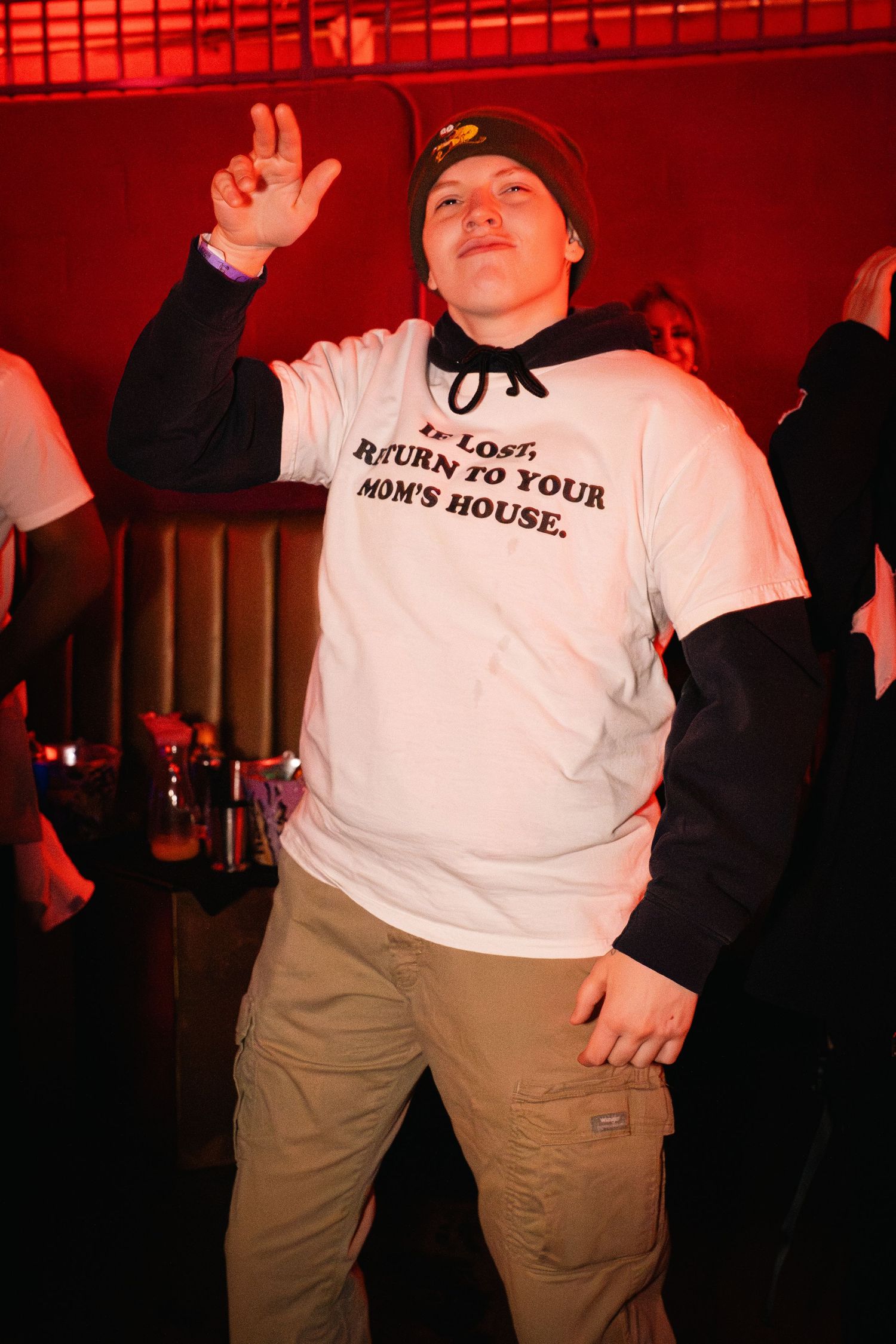 Person in white t-shirt and beanie performing energetically under red stage lighting.