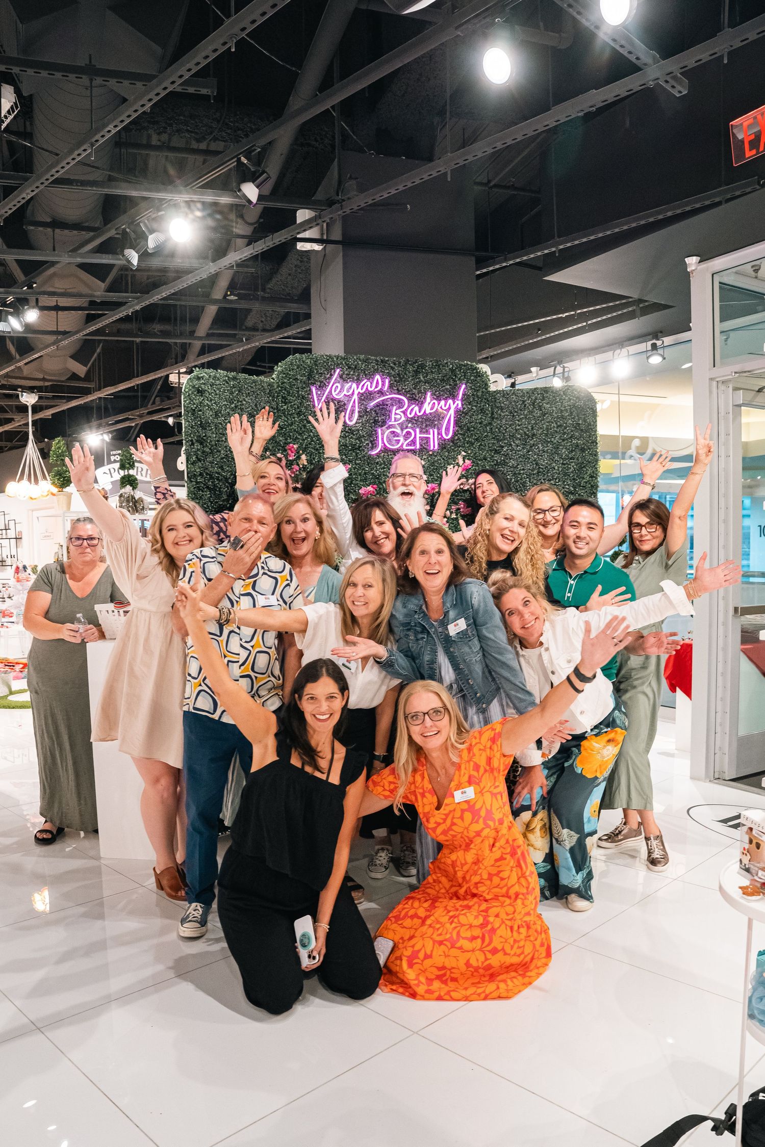 Large group celebration photo with people posing in front of green wall display.