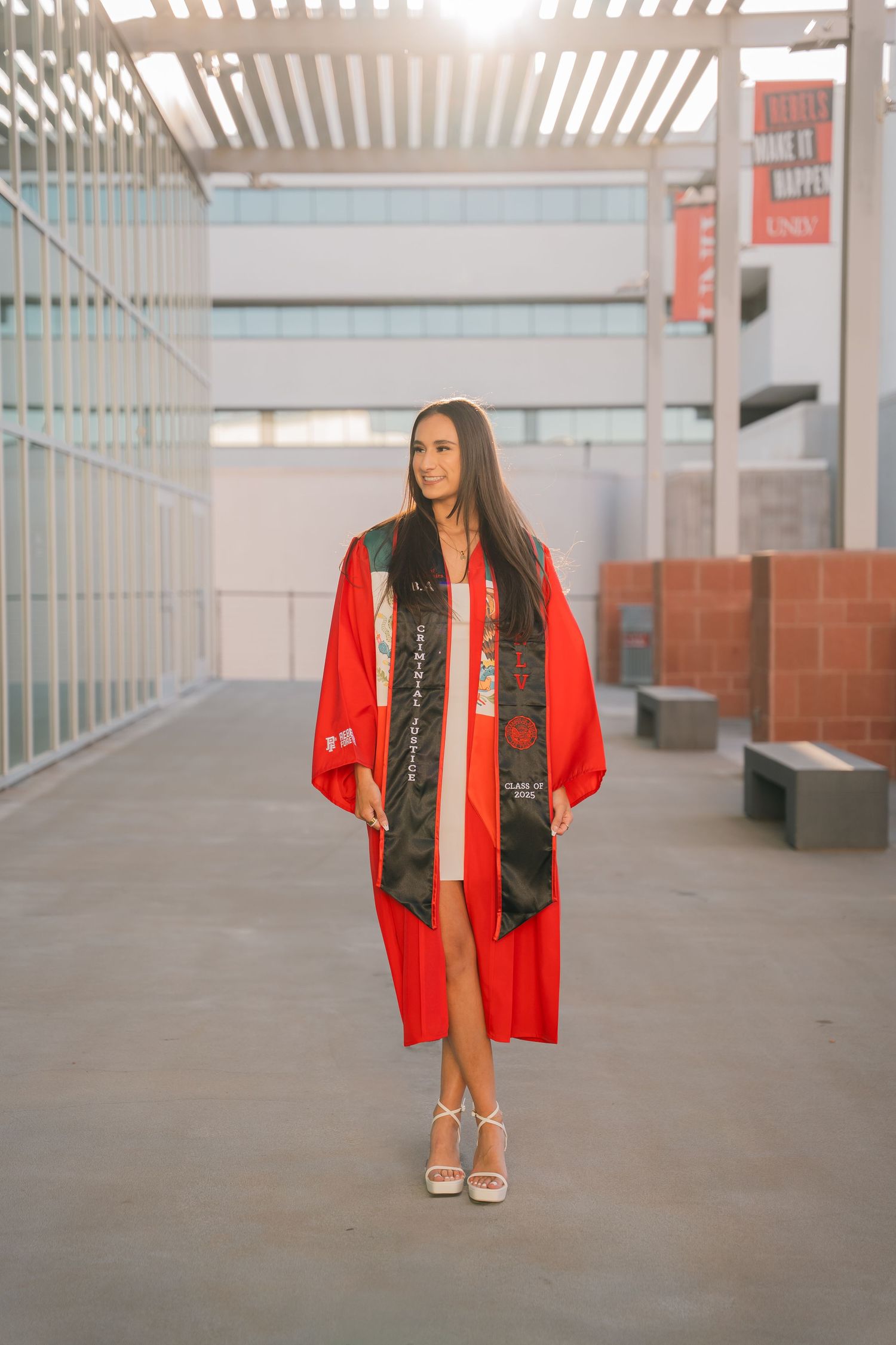 Student in graduation attire stands in modern building hallway with natural lighting.