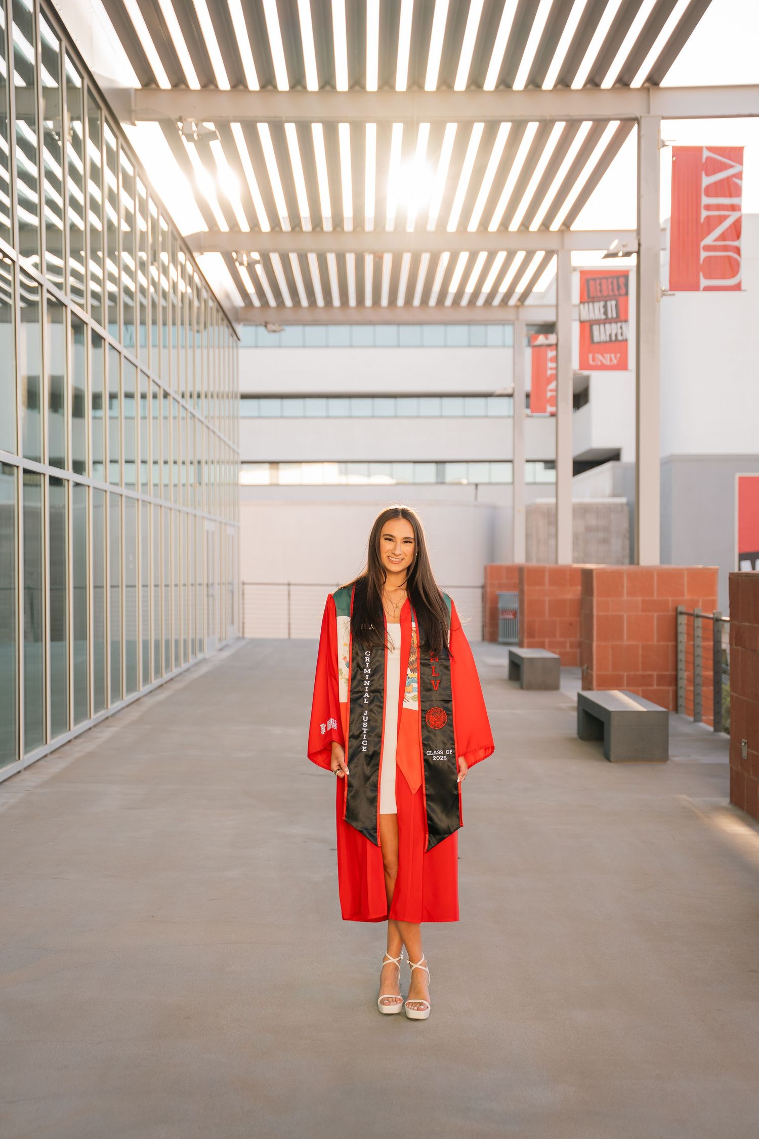 Student in graduation regalia poses in modern university building with slatted ceiling.