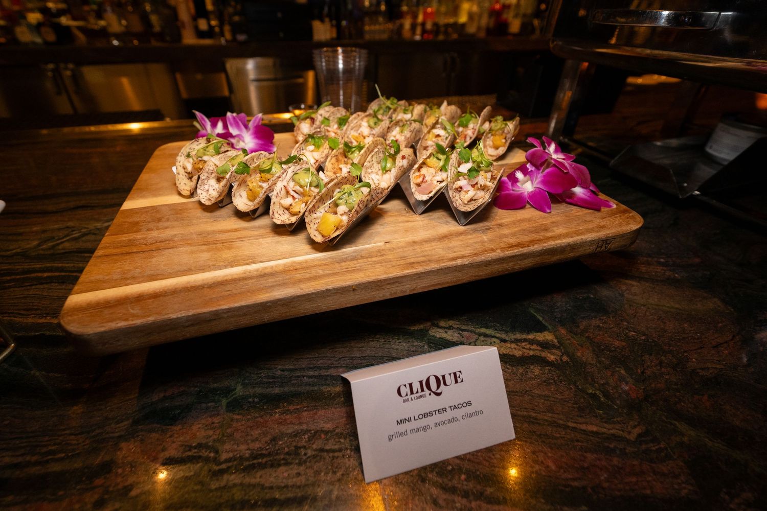 Small appetizers garnished with purple flowers arranged on a wooden serving board with place card.