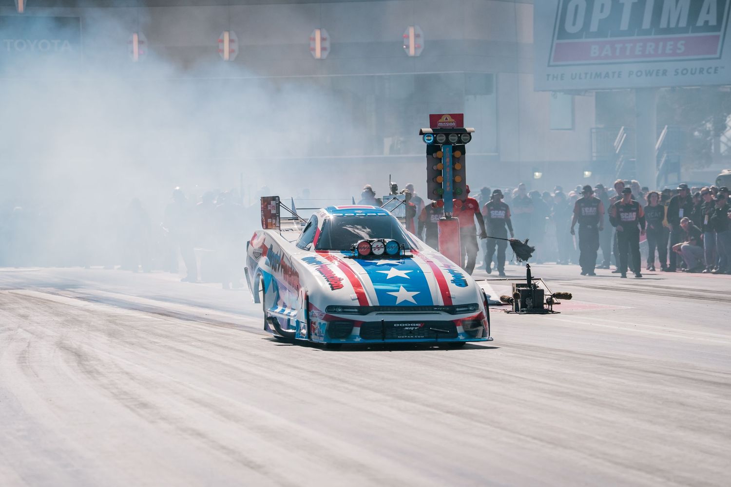 Drag racing car performing a burnout on the track with smoke billowing behind it.